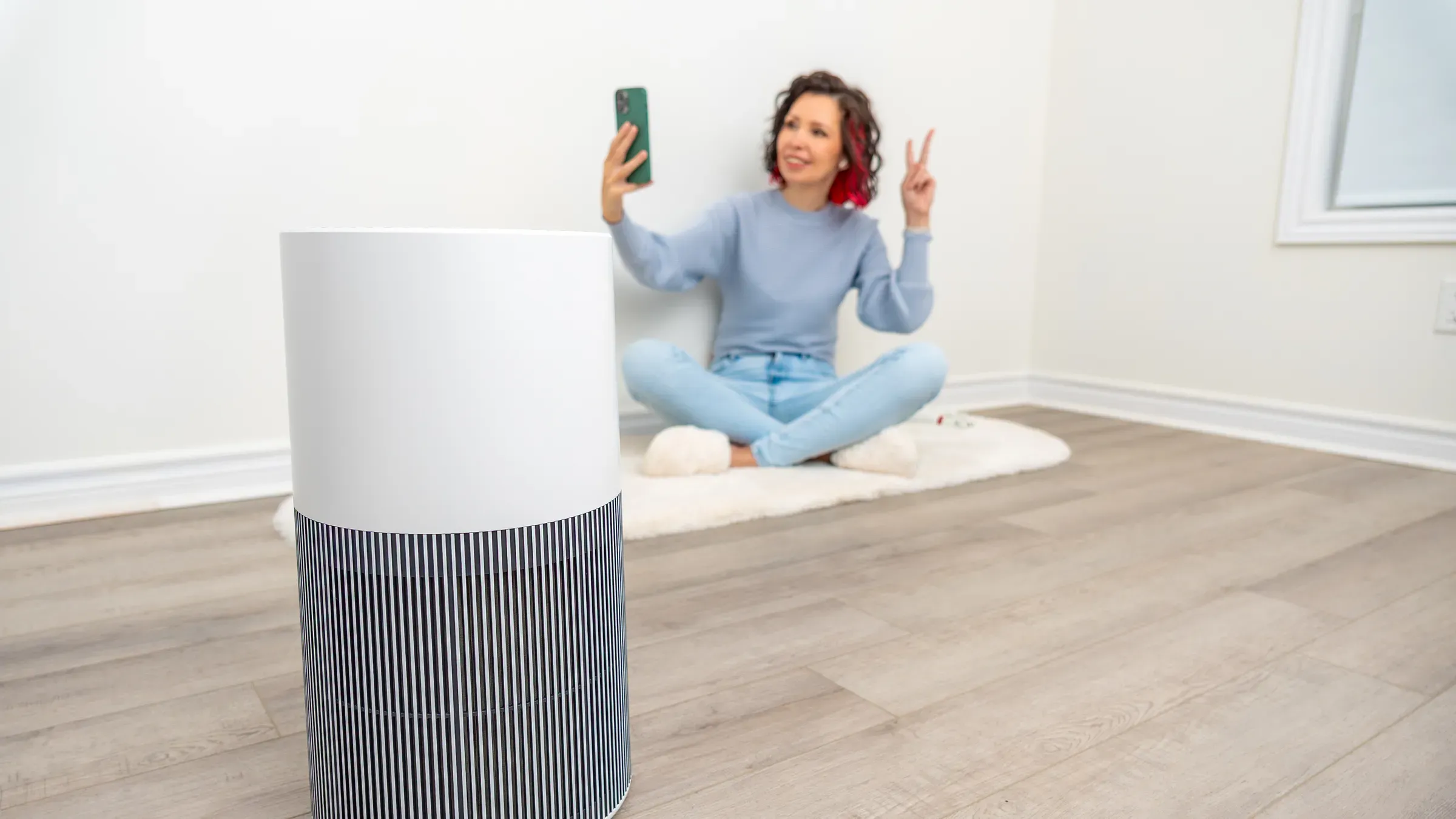 Young woman sitting on floor in cozy room, using smartphone and enjoying fresh air with air purifier,, air purifiers ecommerce