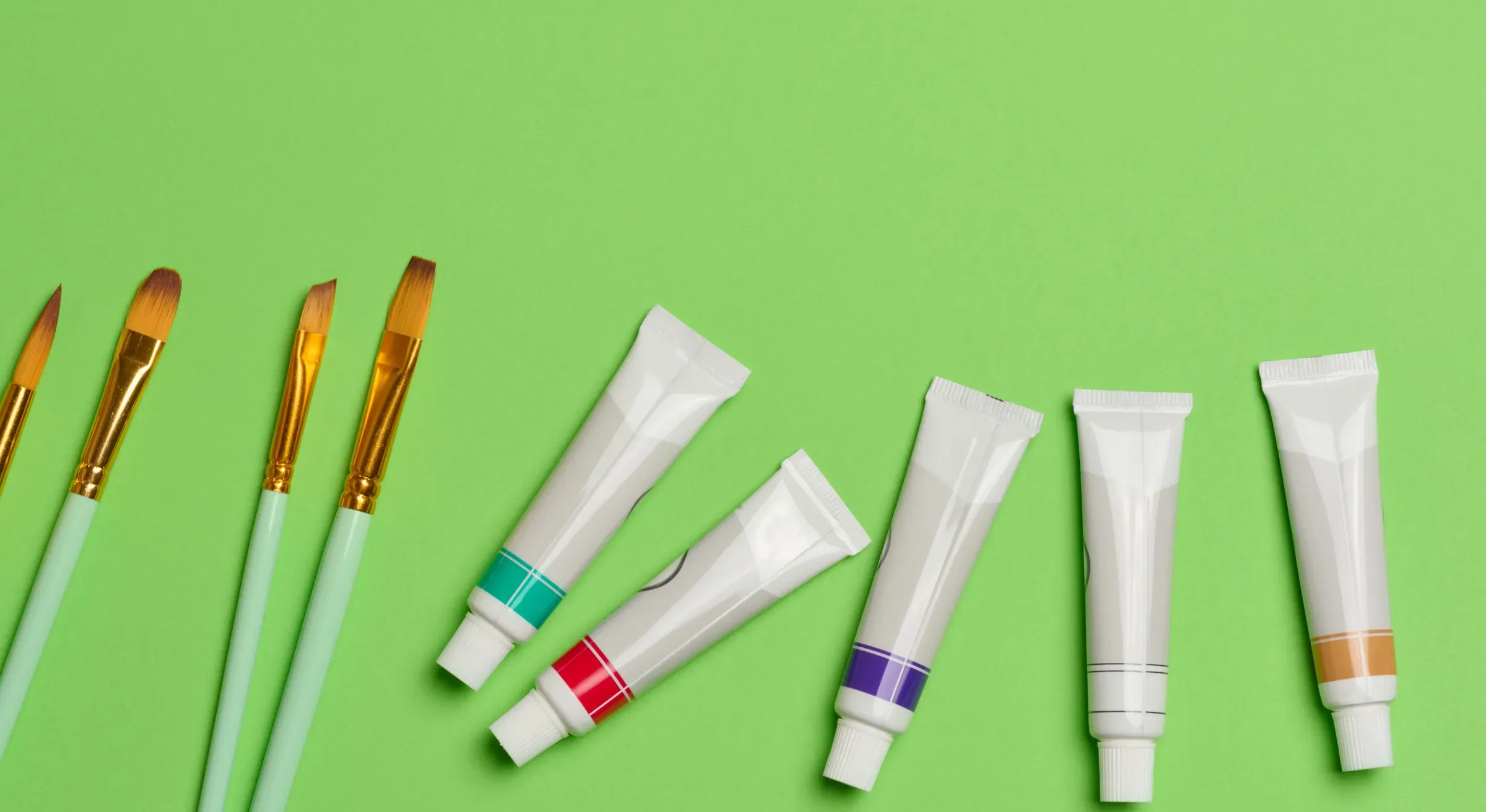 Tubes with oil paint and brushes on a green background, top view, art supplies ecommerce