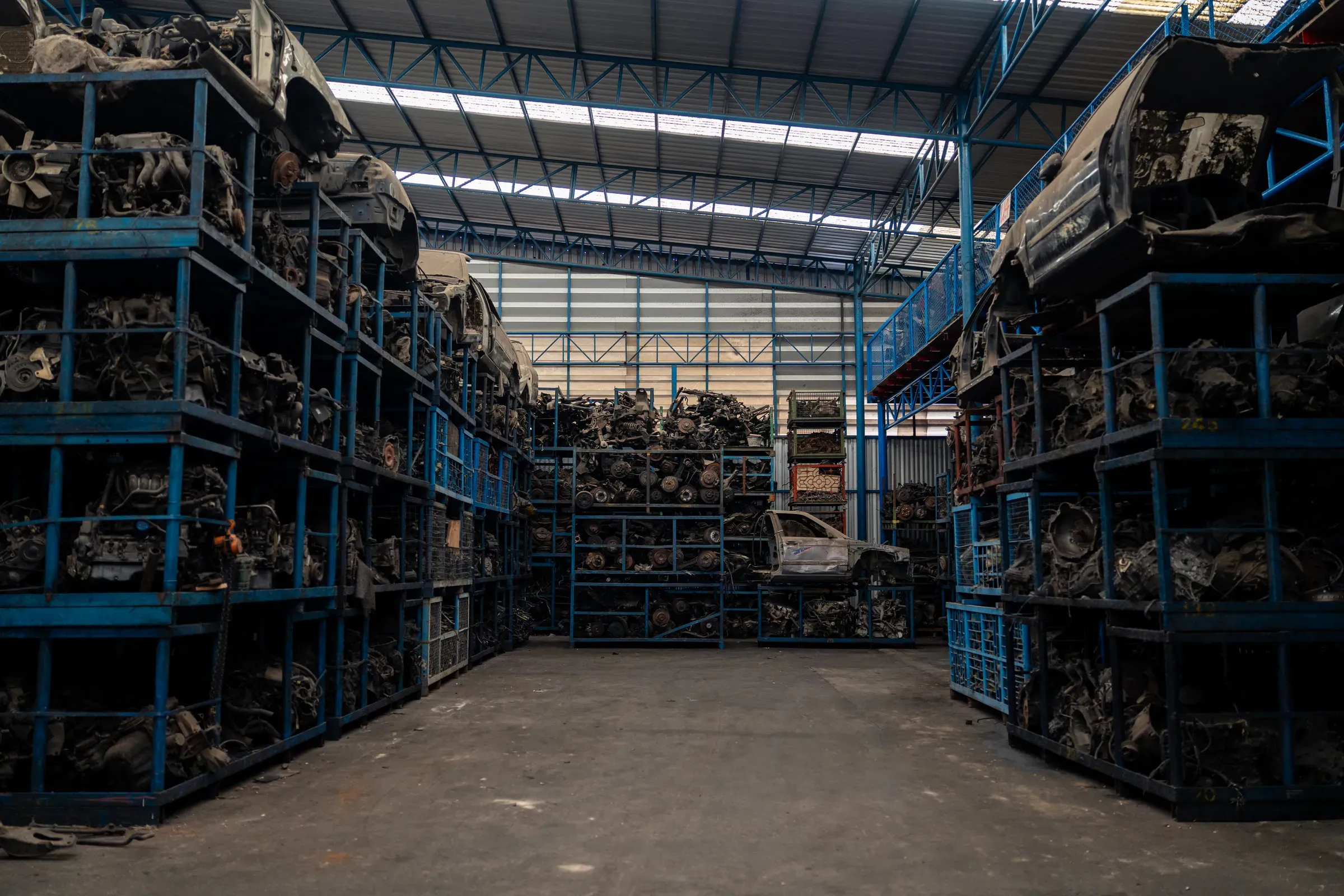 Large industrial warehouse filled with stacked metal shelves containing used automotive parts, engines, and, automotive & powersports ecommerce