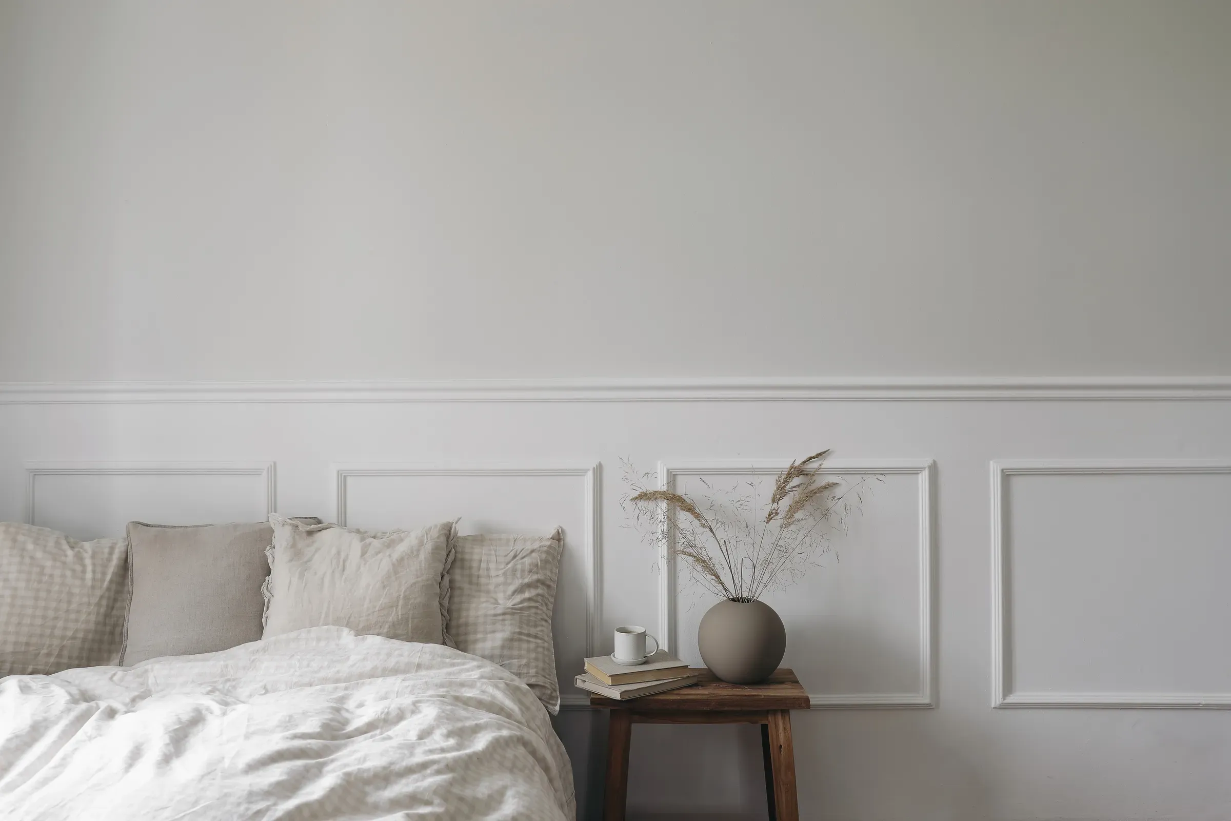Elegant boho bedroom interior. Vintage wooden bedside table. Round modern vase with dry grass. Cup of coffee, bedding & linens ecommerce