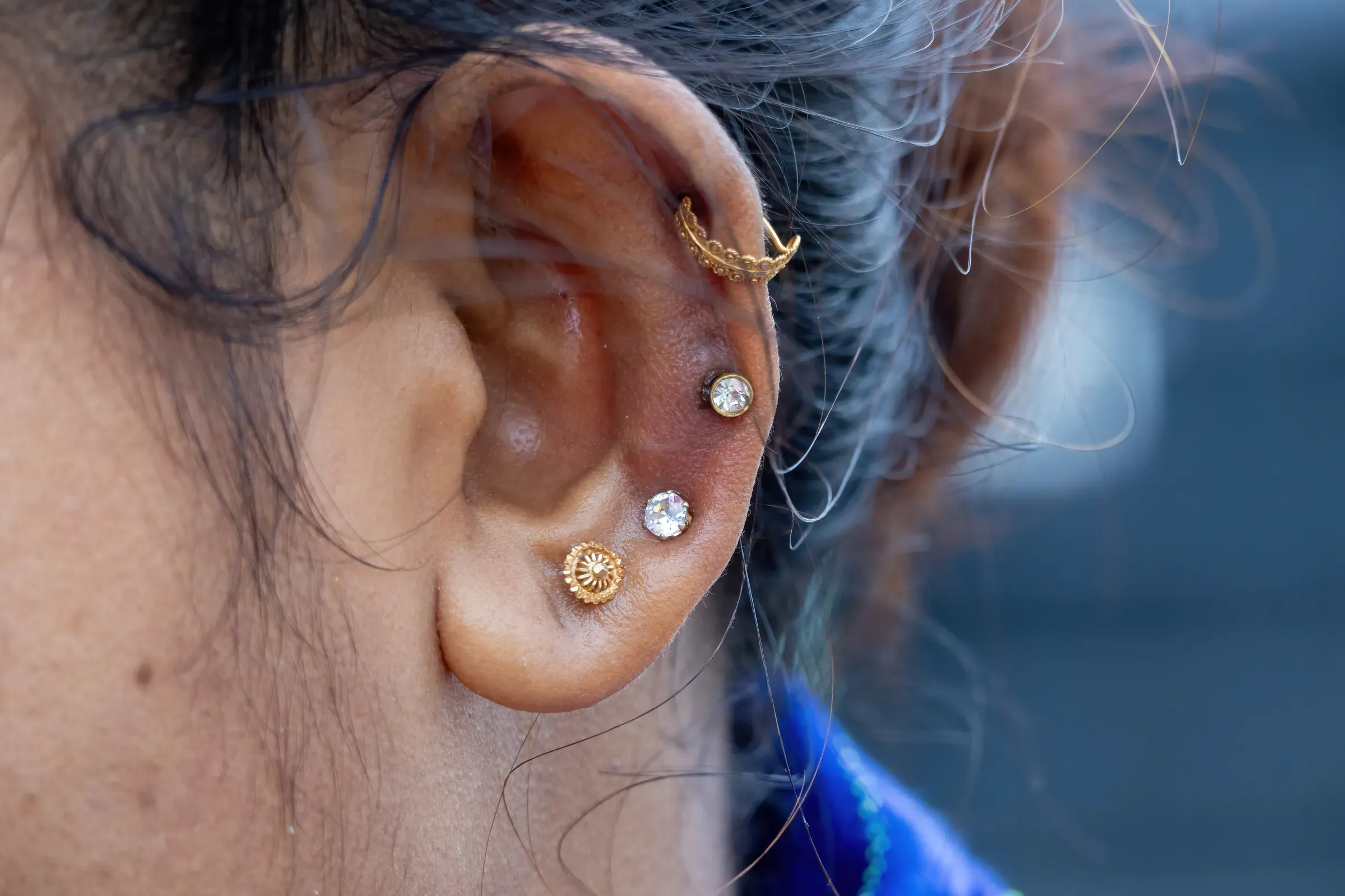 Macro shot of multiple ear piercings including gold studs and a helix hoop on a woman's ear, body & piercing jewelry ecommerce