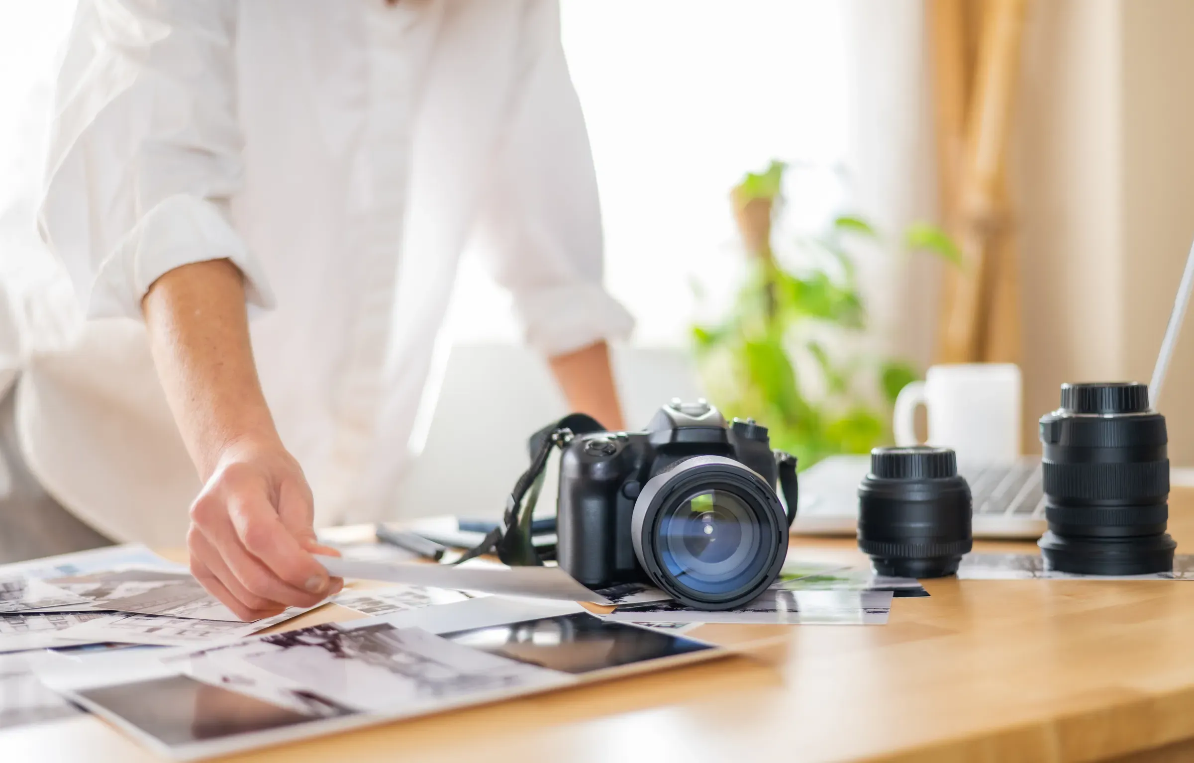 Female photographer selecting printed photos on a desk at her home office, with camera and lenses, cameras & lenses ecommerce