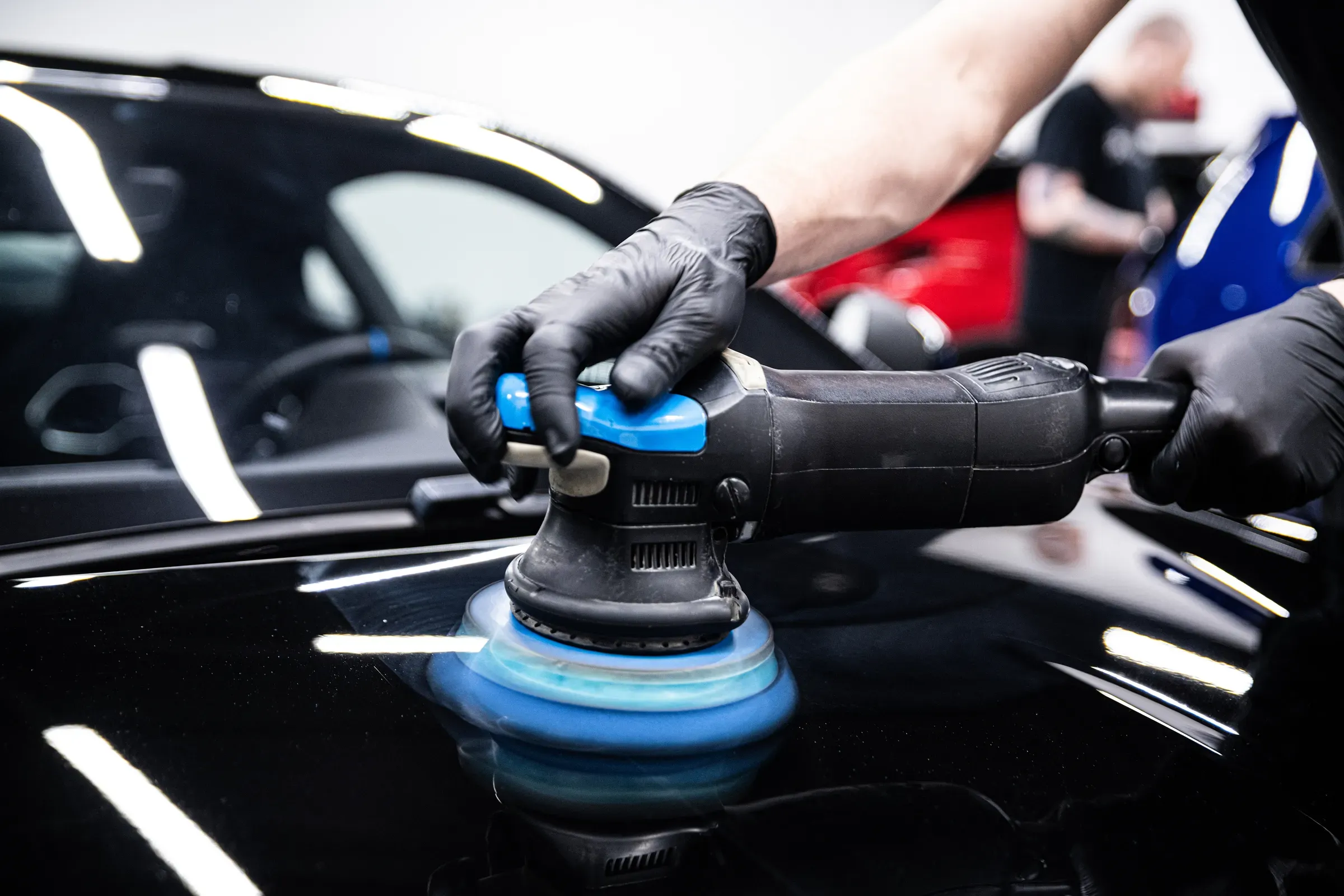 Mechanic wearing black gloves polishing car paint with a machine in a detailing studio, car detailing products ecommerce