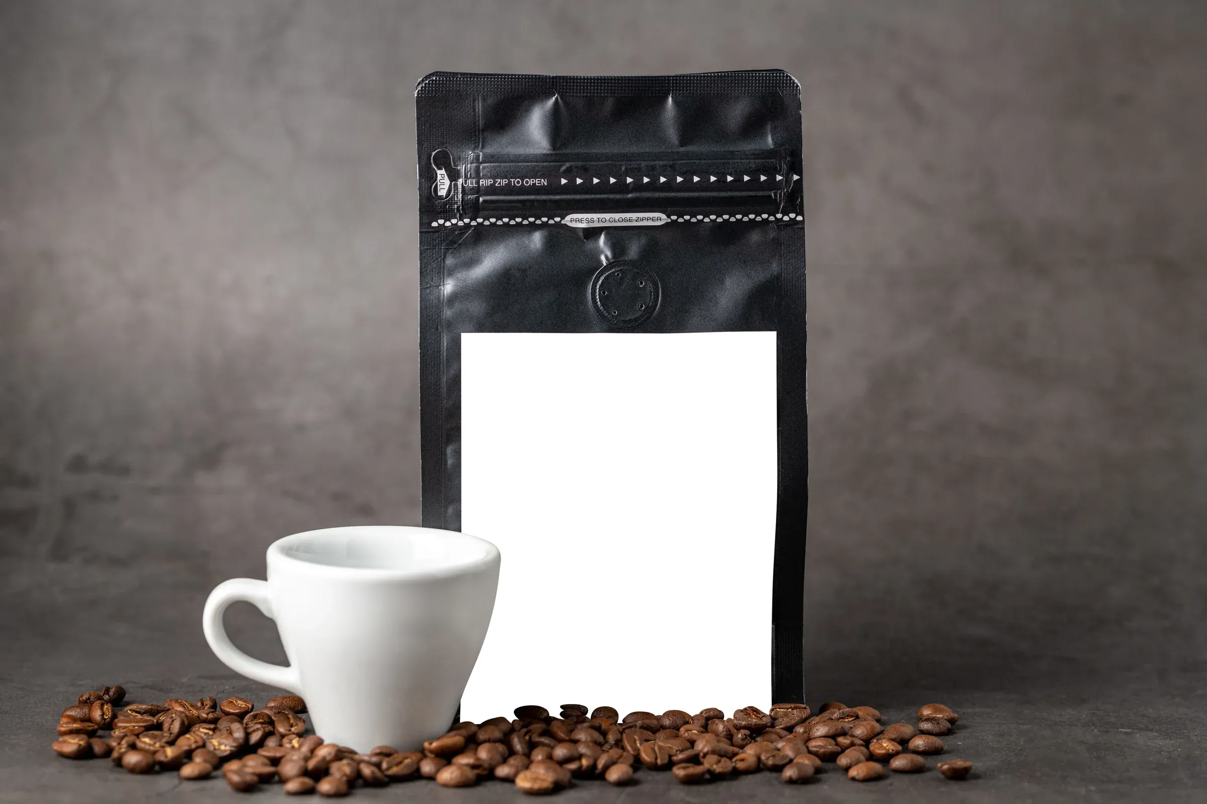 A black coffee bag beside a white espresso cup on a stone surface