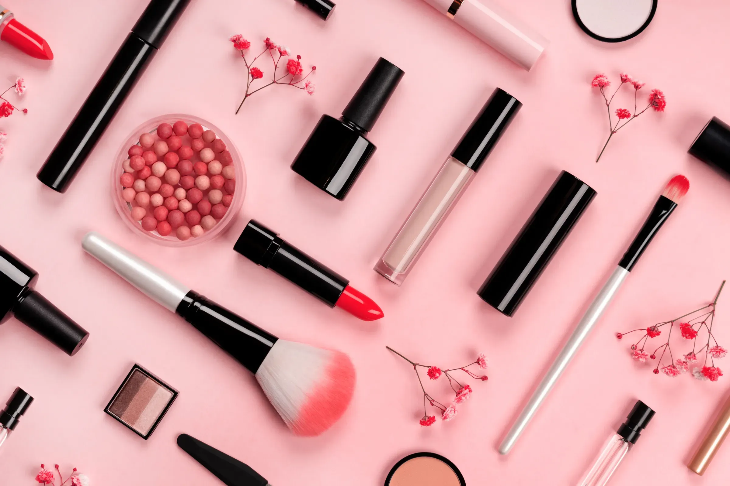 Various cosmetic accessories for makeup and manicure on trendy pastel pink background with red flowers., cosmetics & makeup ecommerce