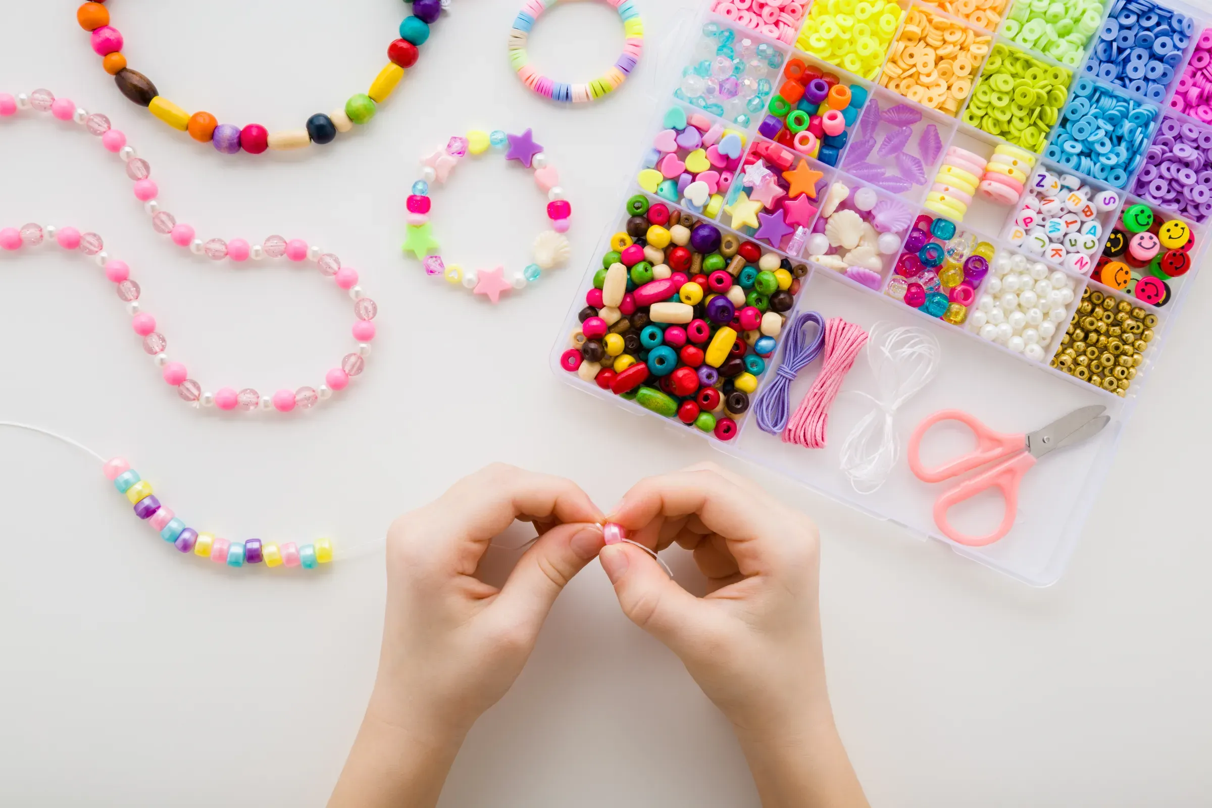 Girl hands making bracelet. Case with different colorful plastic parts on white table background. Creating, craft kits & diy ecommerce