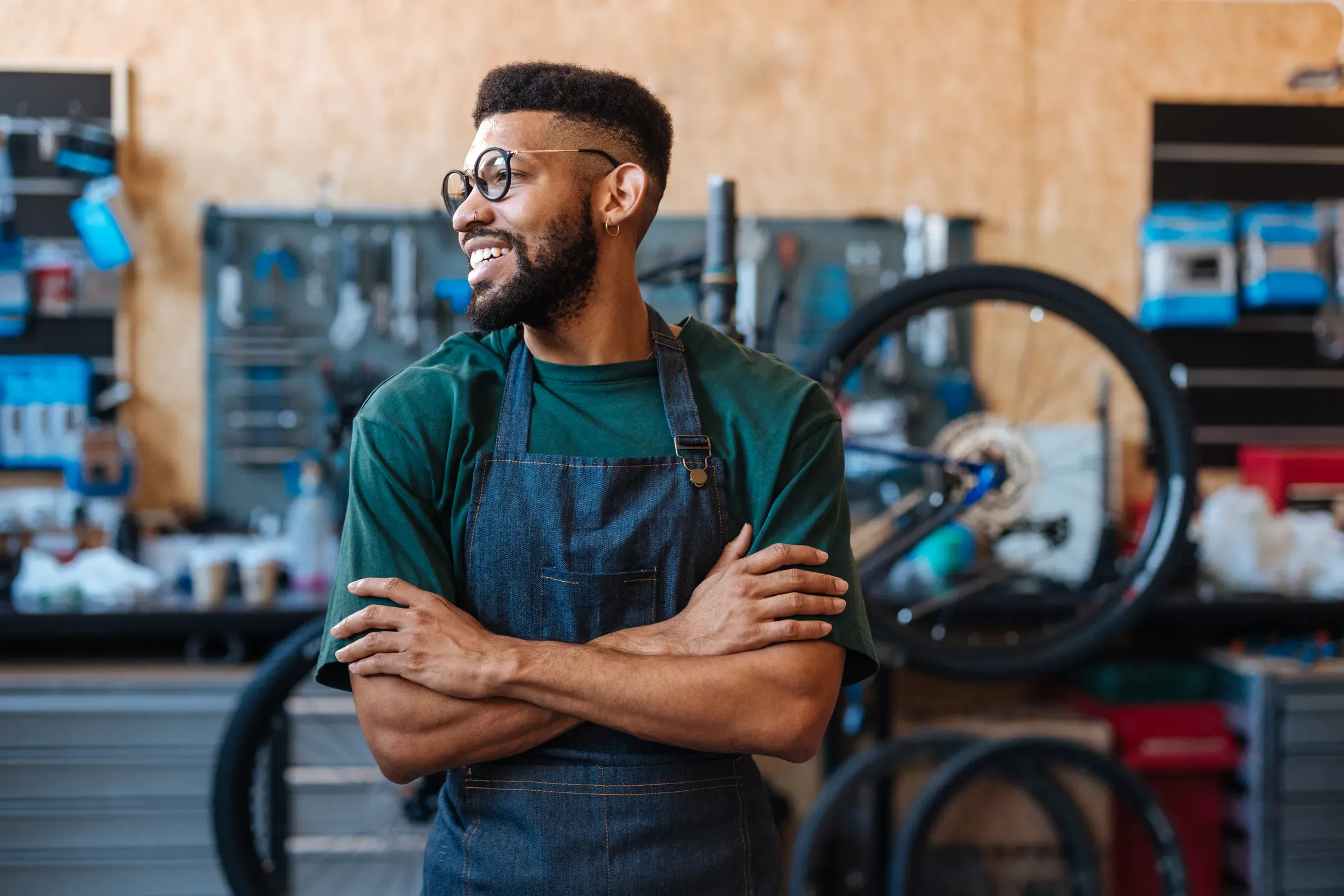 Smiling bicycle mechanic crossing arms in workshop, cycling & bike parts ecommerce