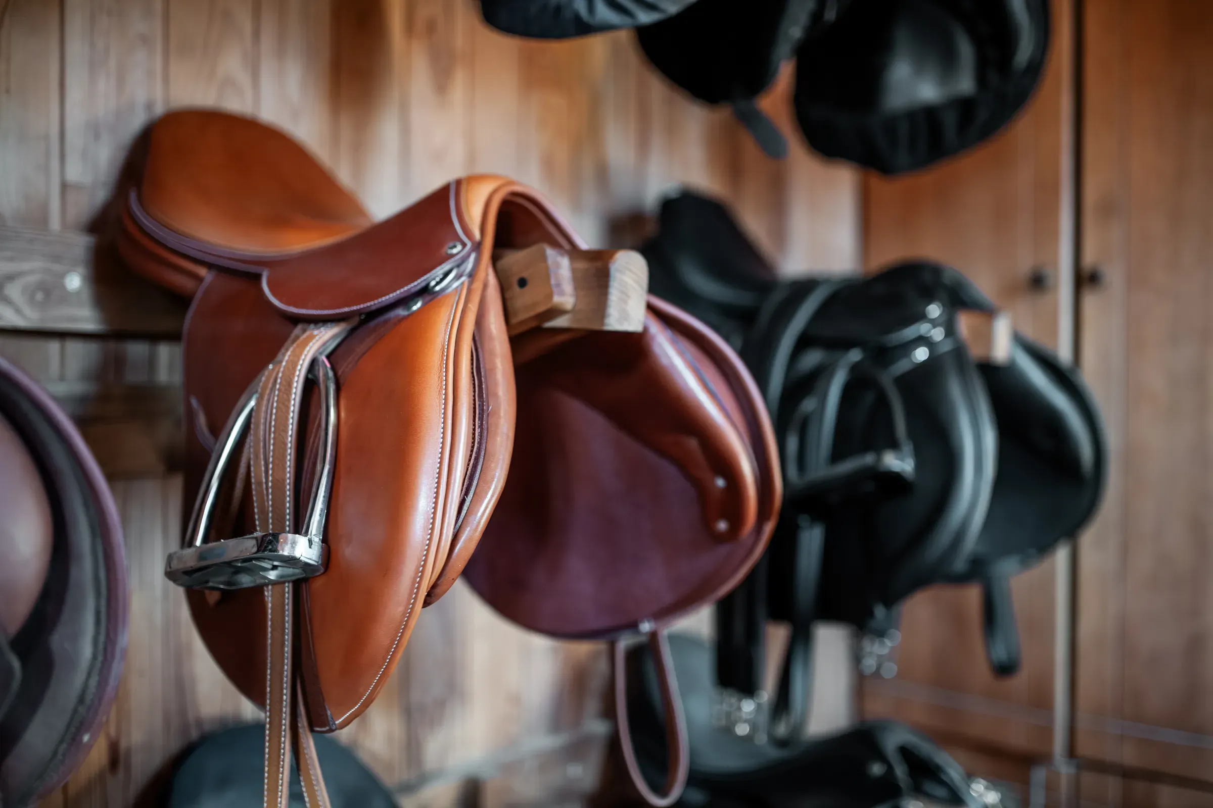 Brown leather saddle hanging on wooden wall at stable or barn, professional equestrian horse riding equipment, horse & equestrian supplies ecommerce