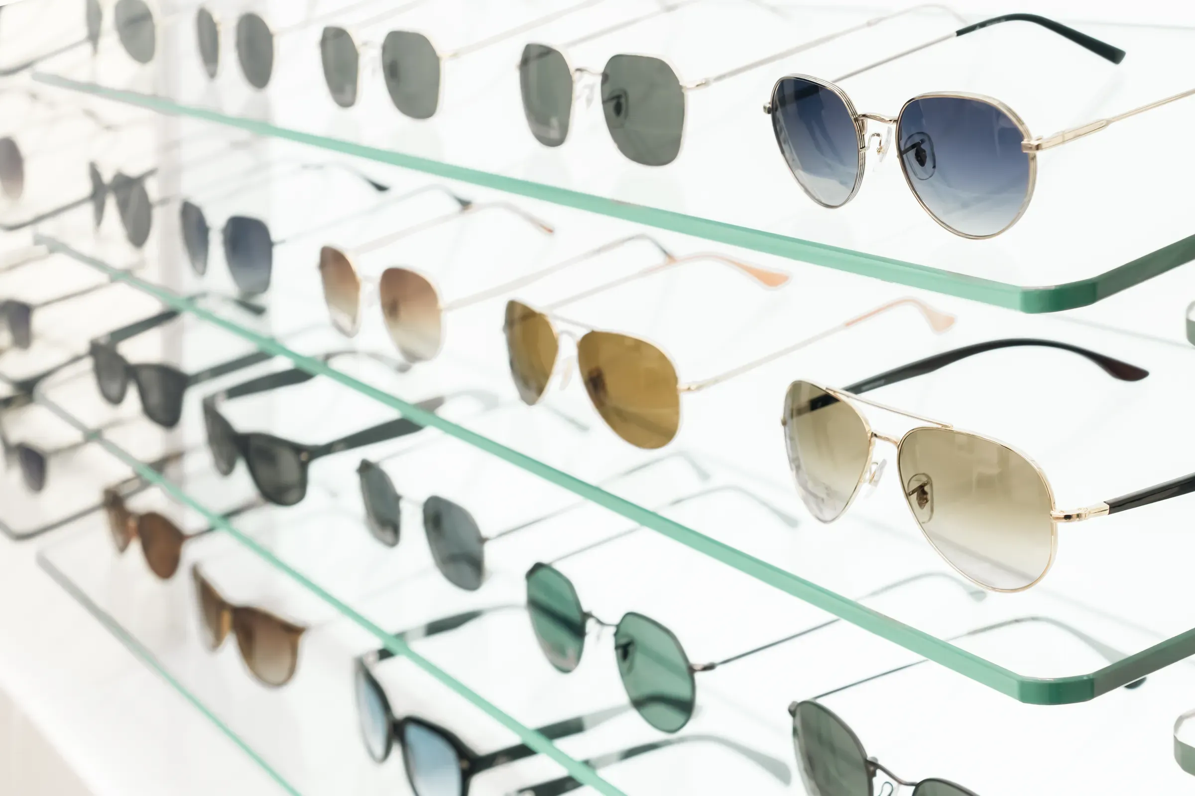 Various sunglasses are arranged neatly on glass shelves in a shop. The display shows multiple styles and, eyewear & sunglasses ecommerce