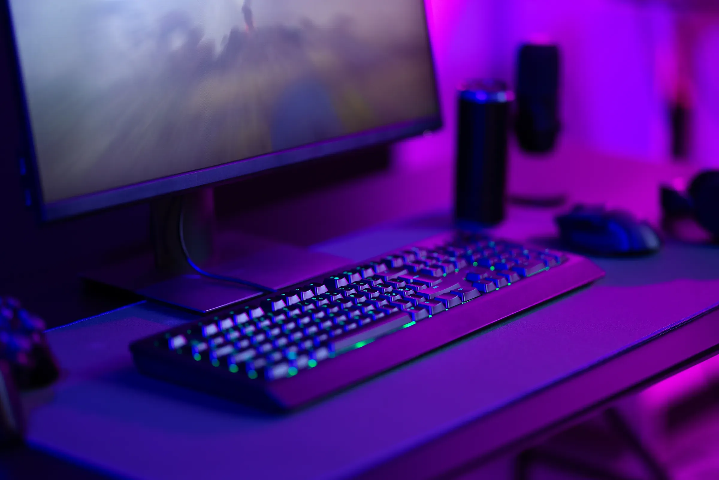 Modern gaming setup with keyboard, mouse, and monitor in a dimly-lit room with purple lighting, gaming peripherals ecommerce