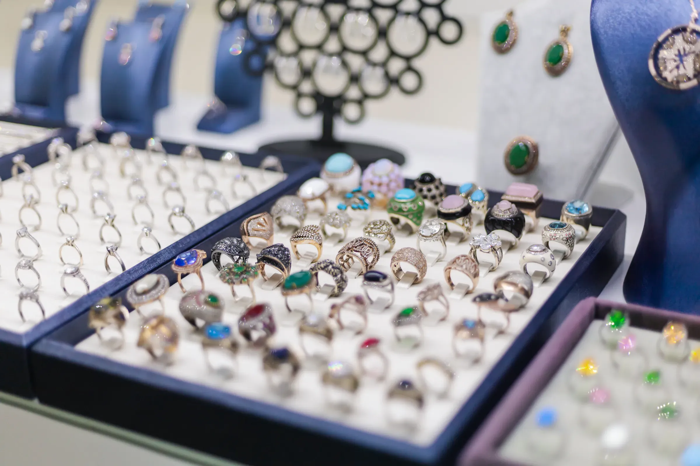 Numerous rings and earrings are arranged on display in a jewelry store. Each piece features unique designs,, gemstone & birthstone jewelry ecommerce