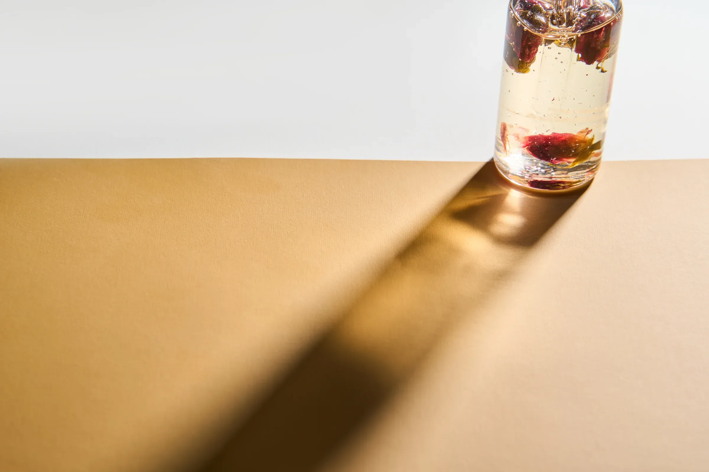 A glass bottle casting a long diagonal shadow on a gold surface