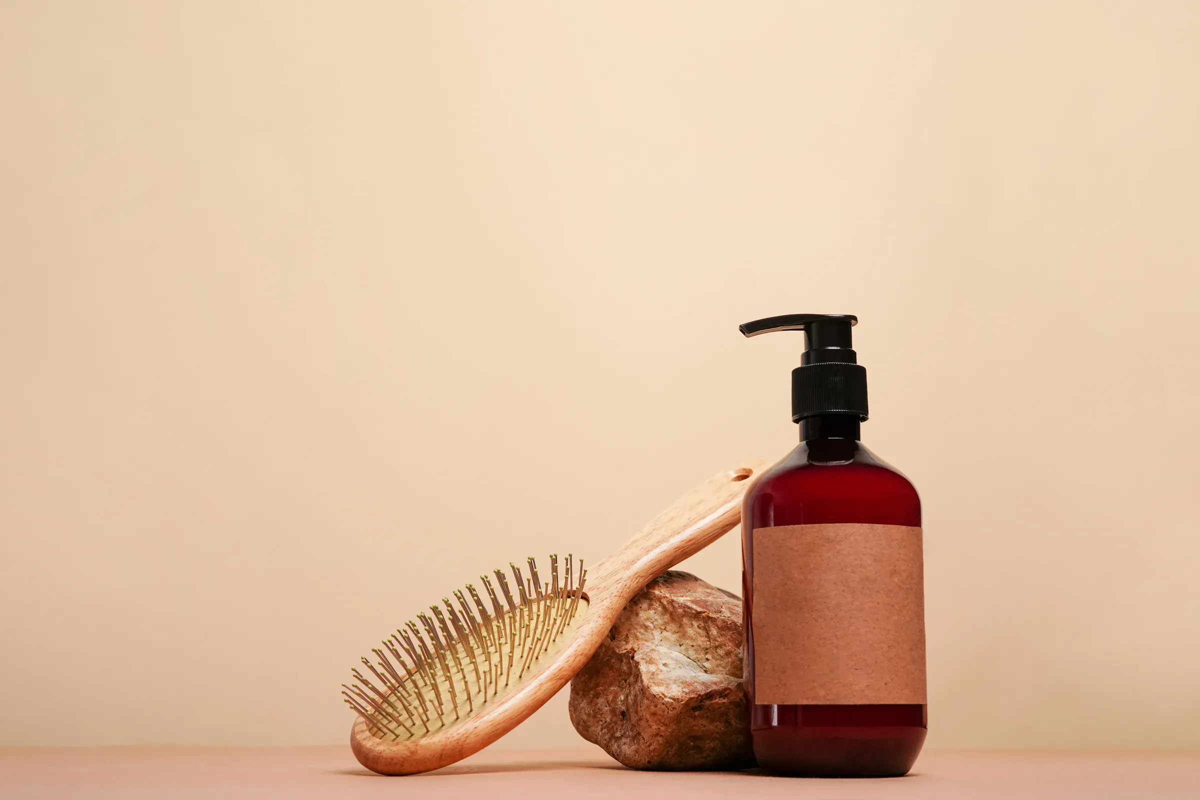 Brown bottle with pump mock up, used for shampoo or conditioner for hair and wood comd near stone on beige, haircare ecommerce