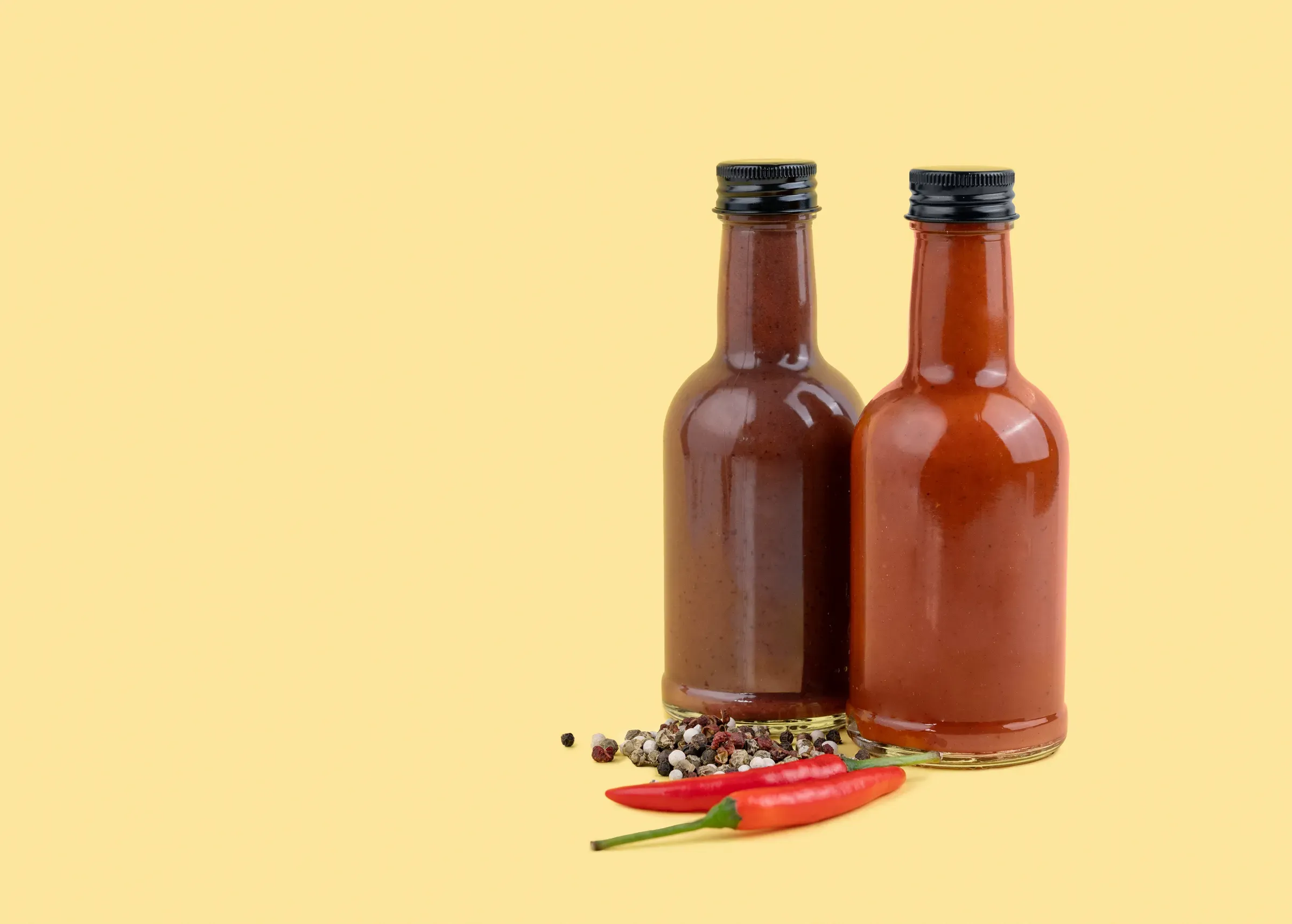Two spicy sauce bottles with chili peppers and spices on yellow background, hot sauce & condiments ecommerce