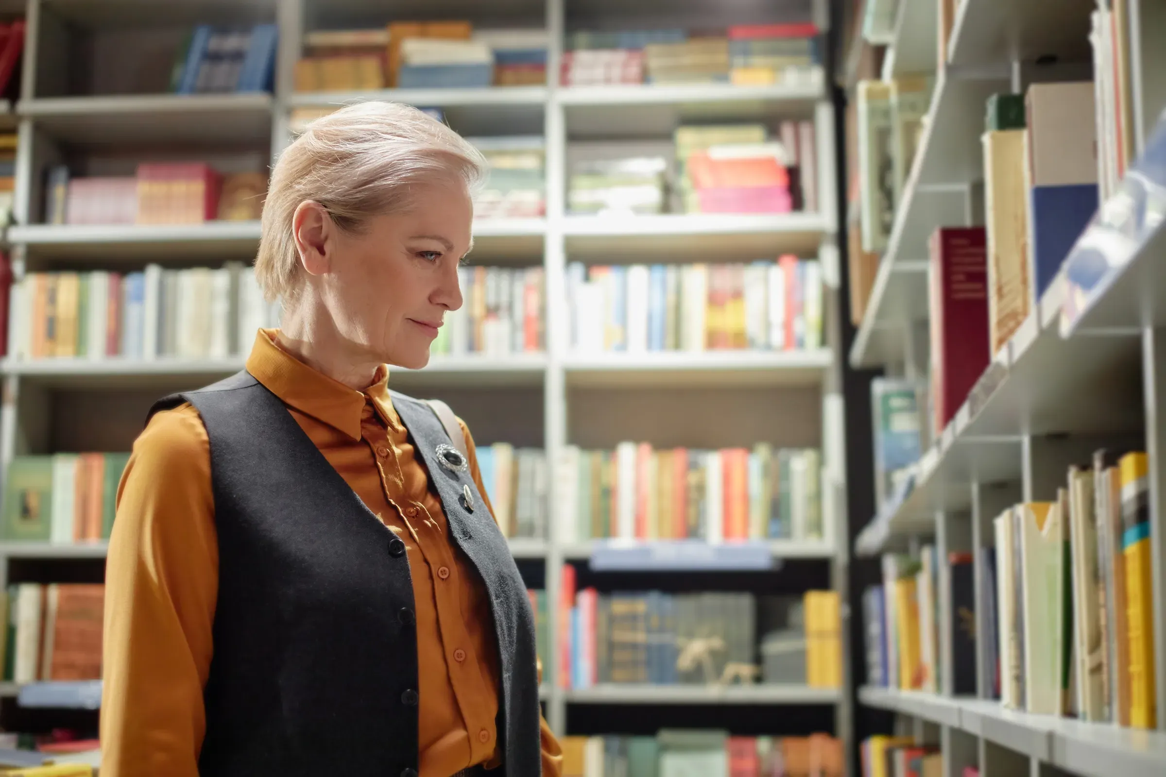 Middle Aged Caucasian Woman Browsing Bookshelves in Library Setting, independent publishers & bookshops ecommerce
