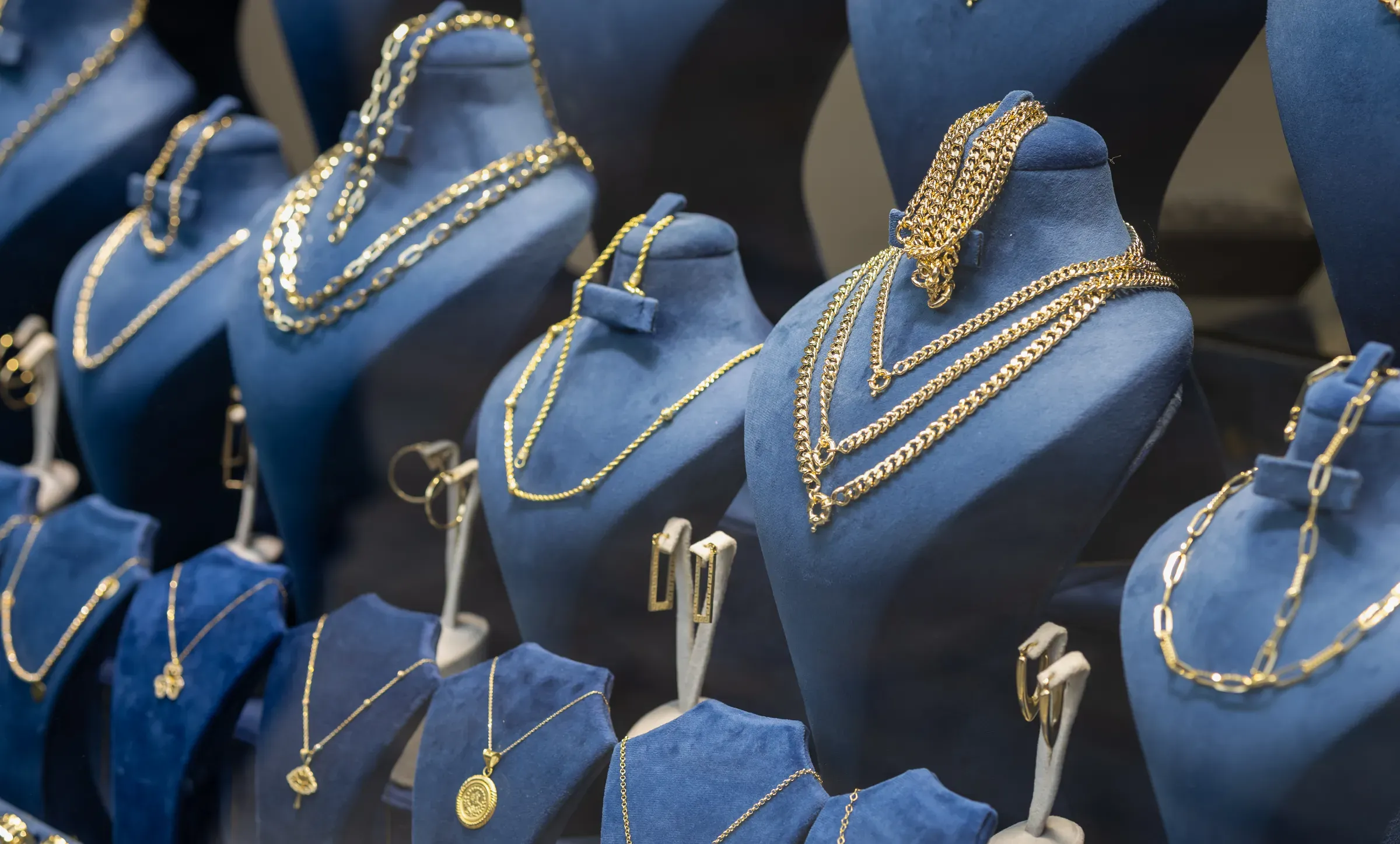 Luxurious display of elegant gold necklaces and jewelry on blue velvet busts in a high-end boutique window, jewelry ecommerce