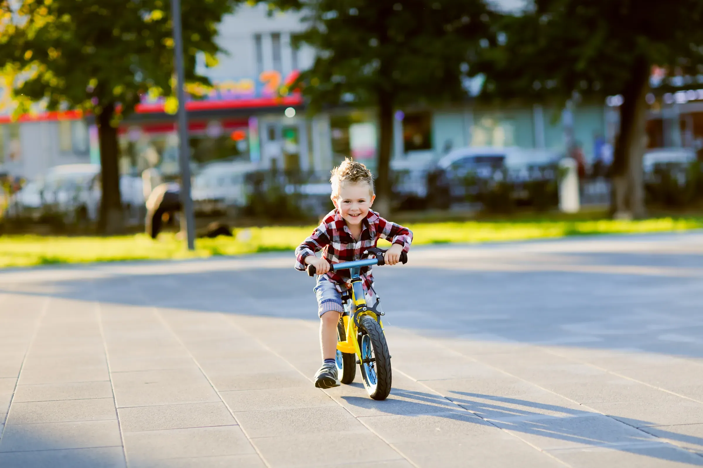 Stylish European boy in shirt and jeans rides balance bike on asphalt. Child riding without helmet, kids bikes & ride-ons ecommerce