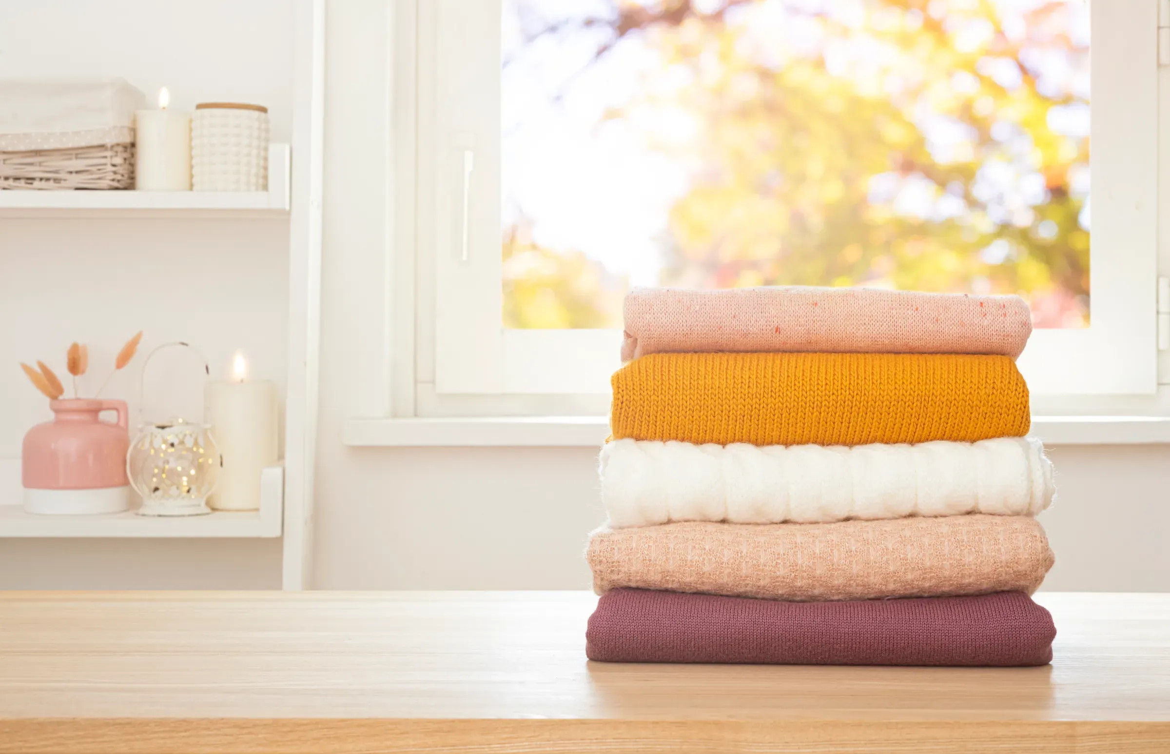 Stack of colorful folded clothes on wooden table with background of window and household shelf, kids clothing ecommerce