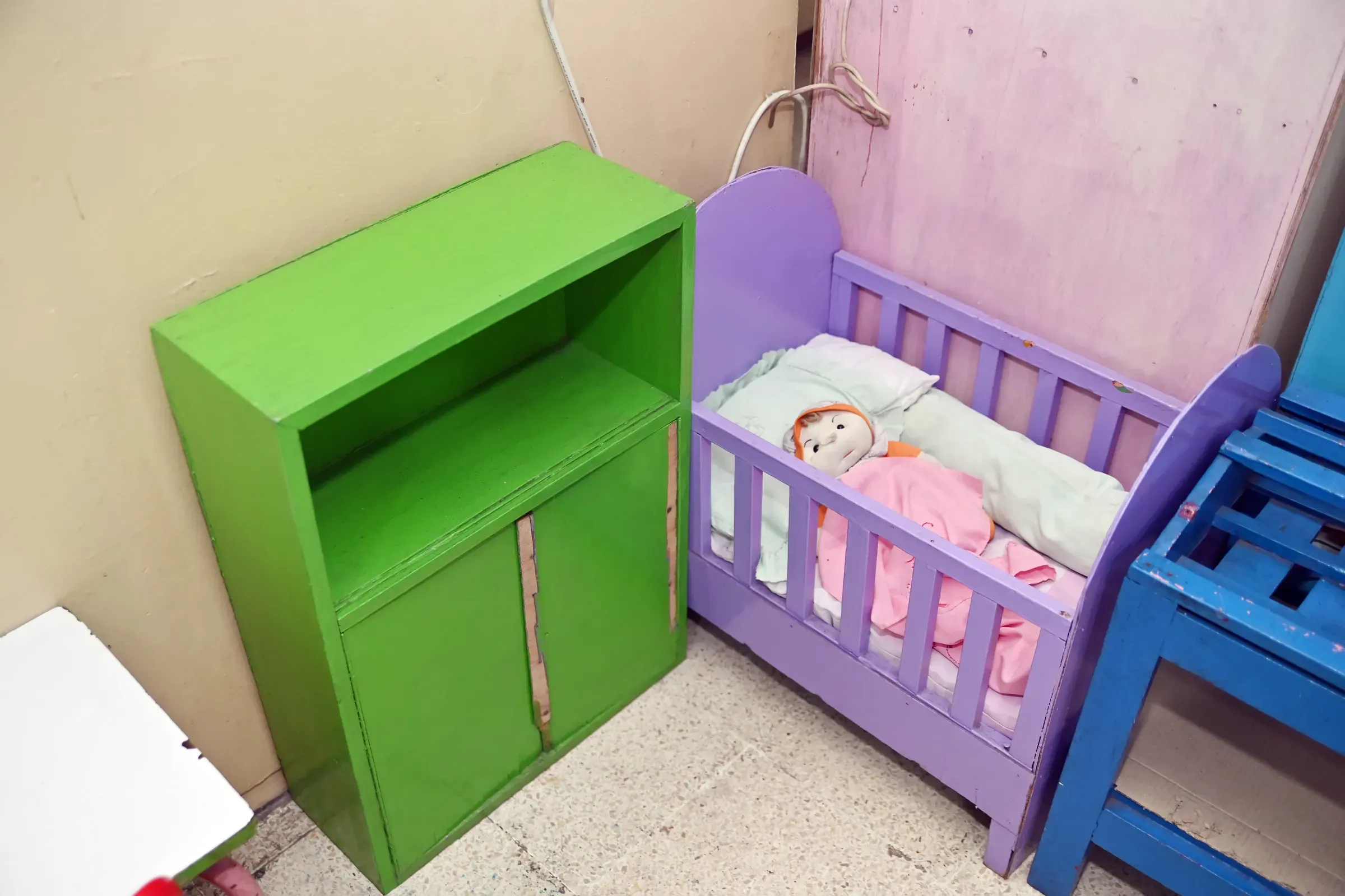 A corner of a playroom or nursery showing a bright green wooden storage cabinet next to a small purple toy, kids furniture & nursery ecommerce