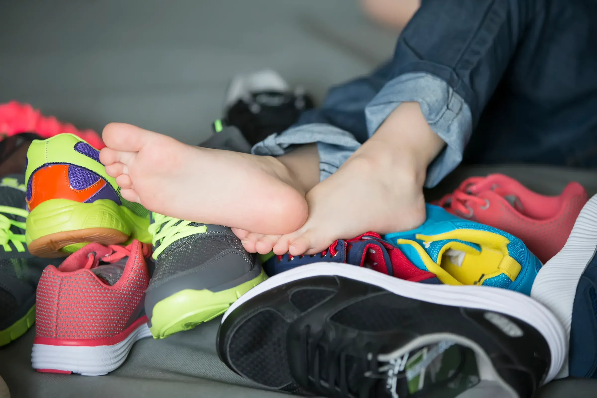 Bare feet in a pile of shoes. Children's foot on the background of sneakers. Foot and shoes, kids shoes ecommerce