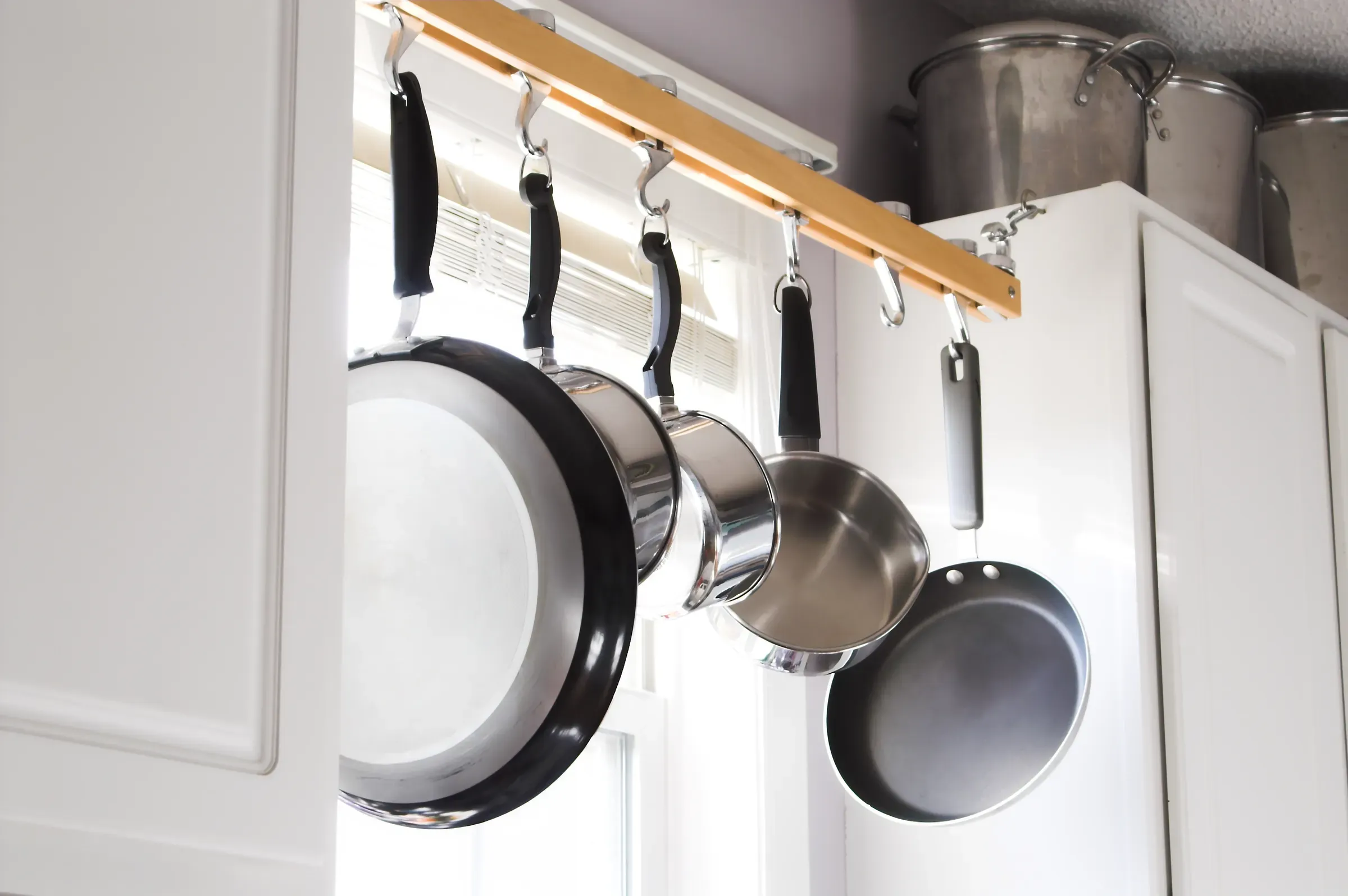 Stainless steel pots and pans hanging from hooks in kitchen, kitchenware & cookware ecommerce