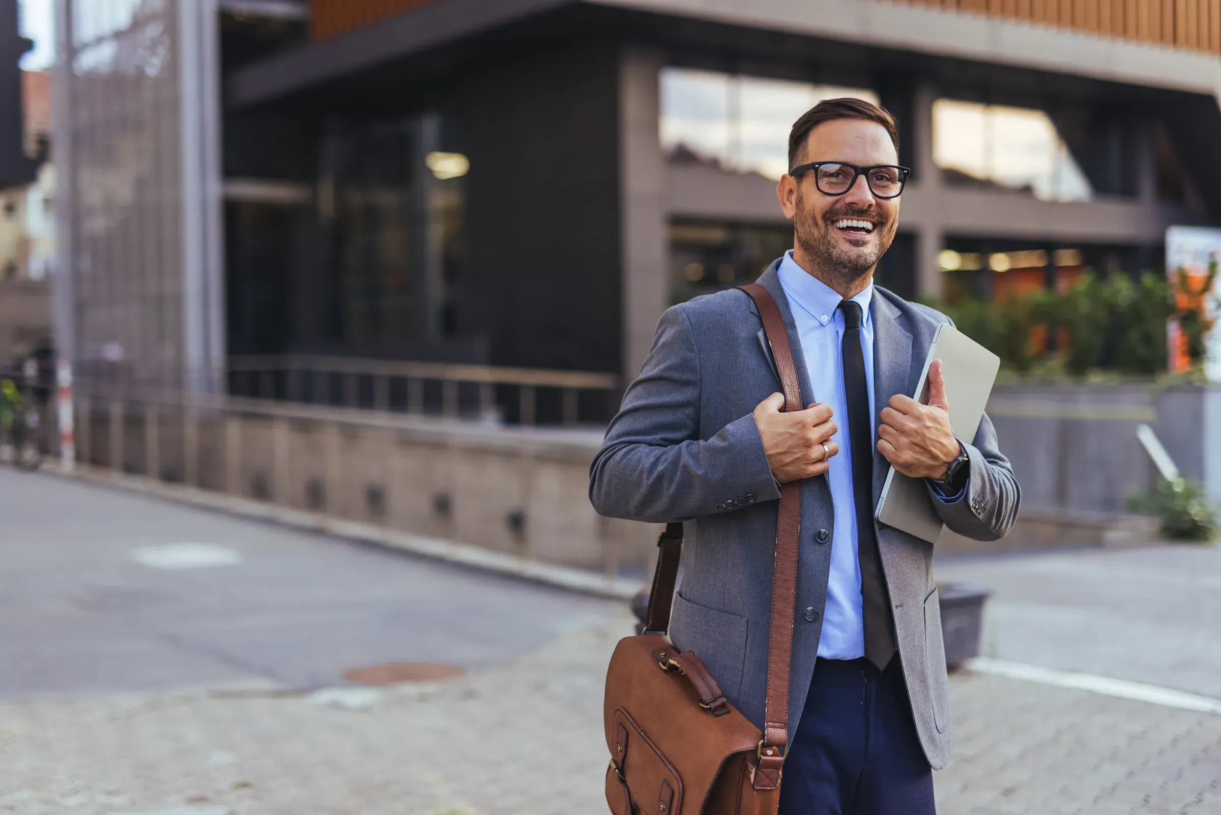 Smiling Businessman Carrying Laptop and Leather Briefcase Outside Modern Office Building, Confident, laptop bags & briefcases ecommerce