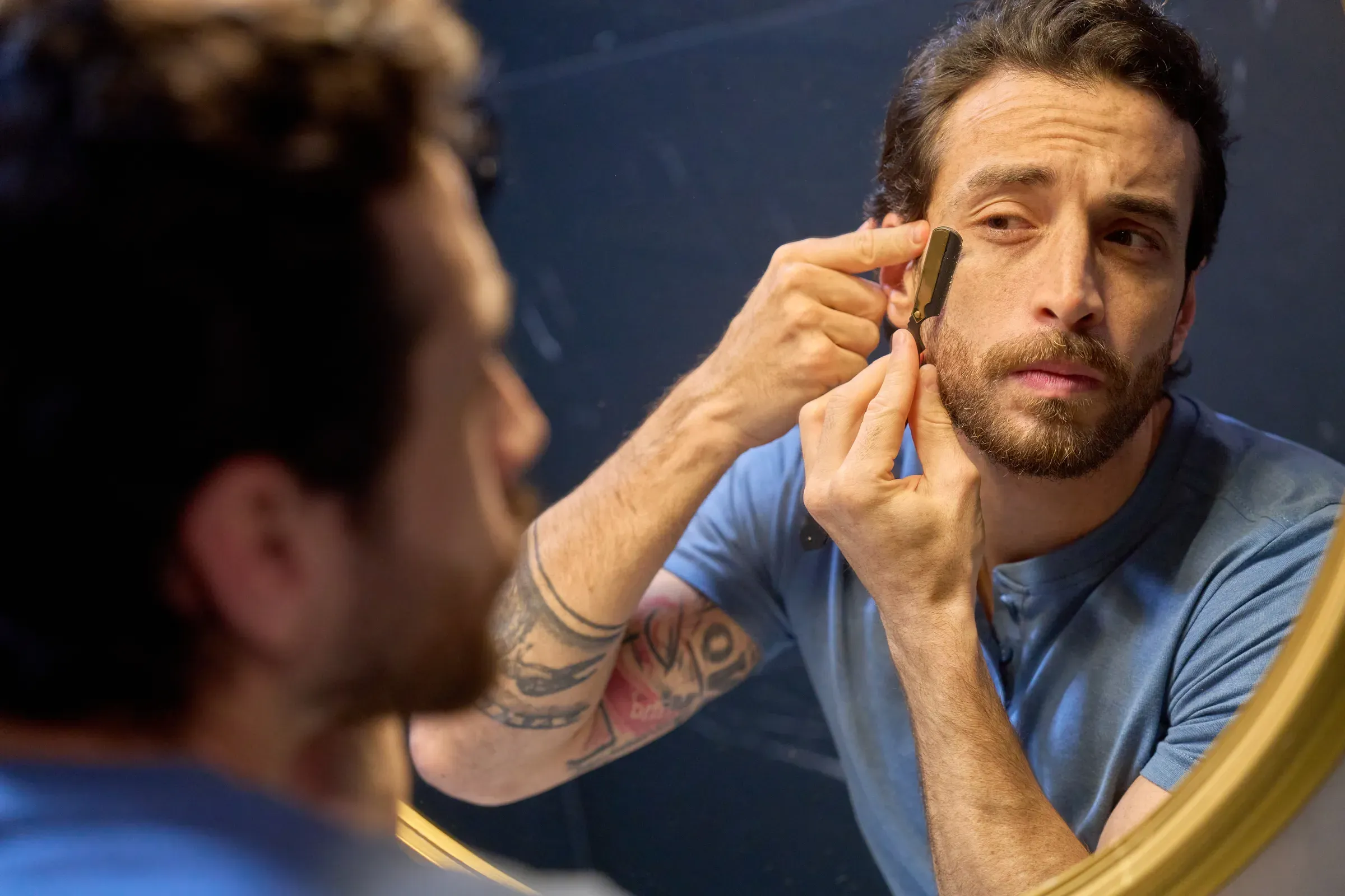 Man shaving beard with straight razor in mirror, men's grooming ecommerce