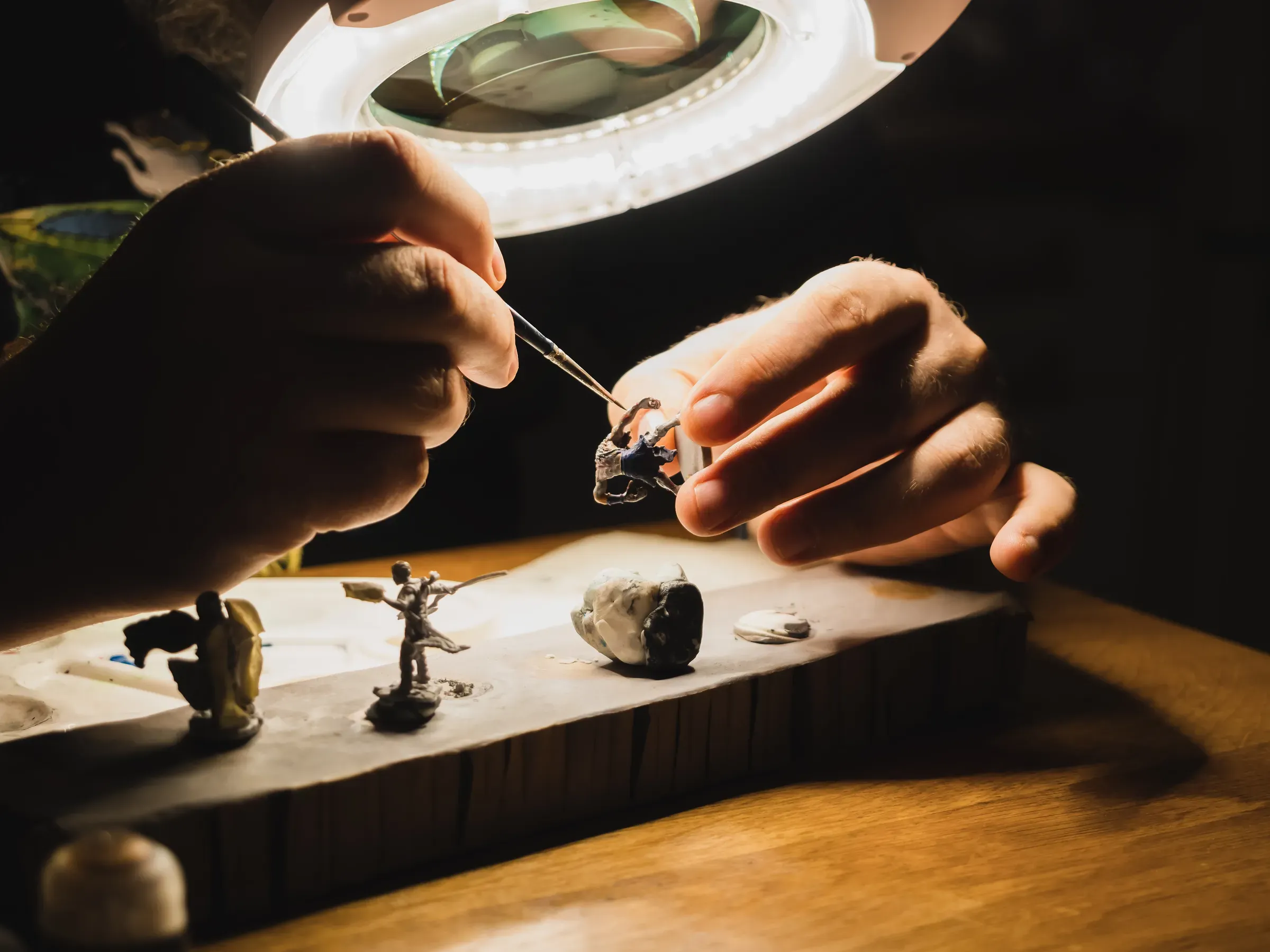 Human hands painting under the lamp with light and magnifying glass plastic minifigures for board games ,, model kits & miniatures ecommerce
