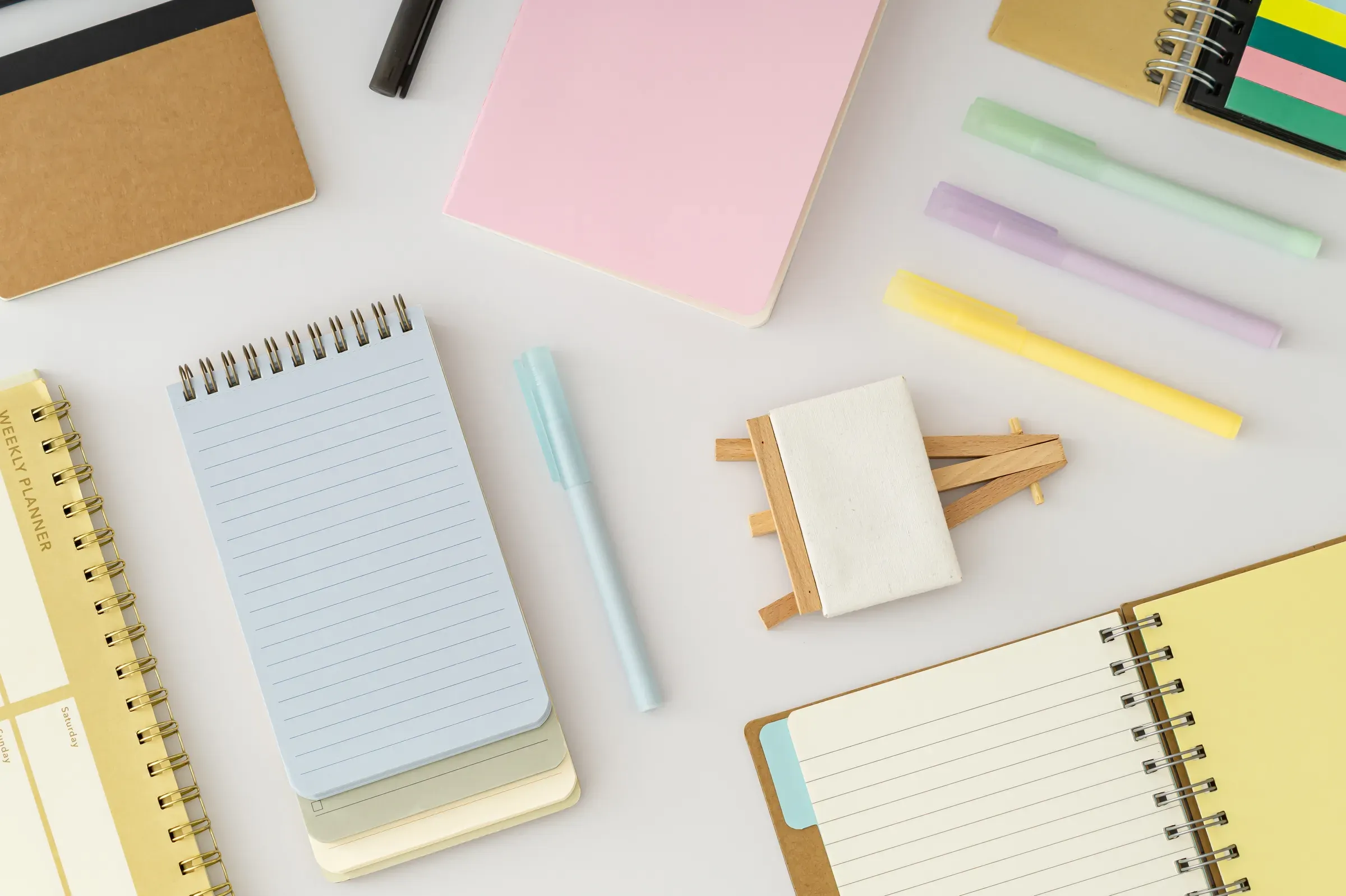 Office desk flat lay with notebooks, planner and colorful pens on white background. Planning, notebooks & pens ecommerce