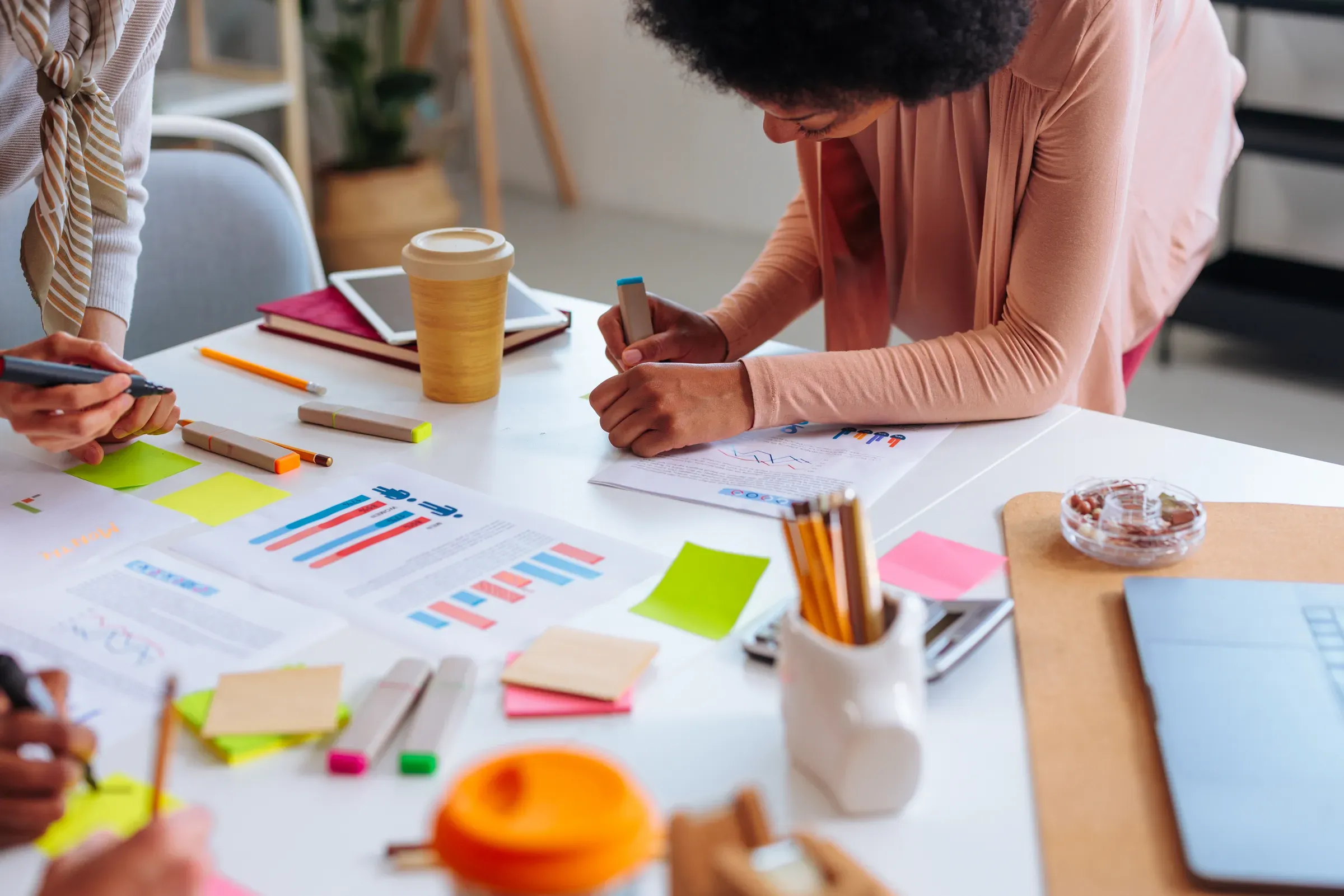 Office desk with stationery and paper graphs while female colleagues use it for calculations for project, office supplies ecommerce
