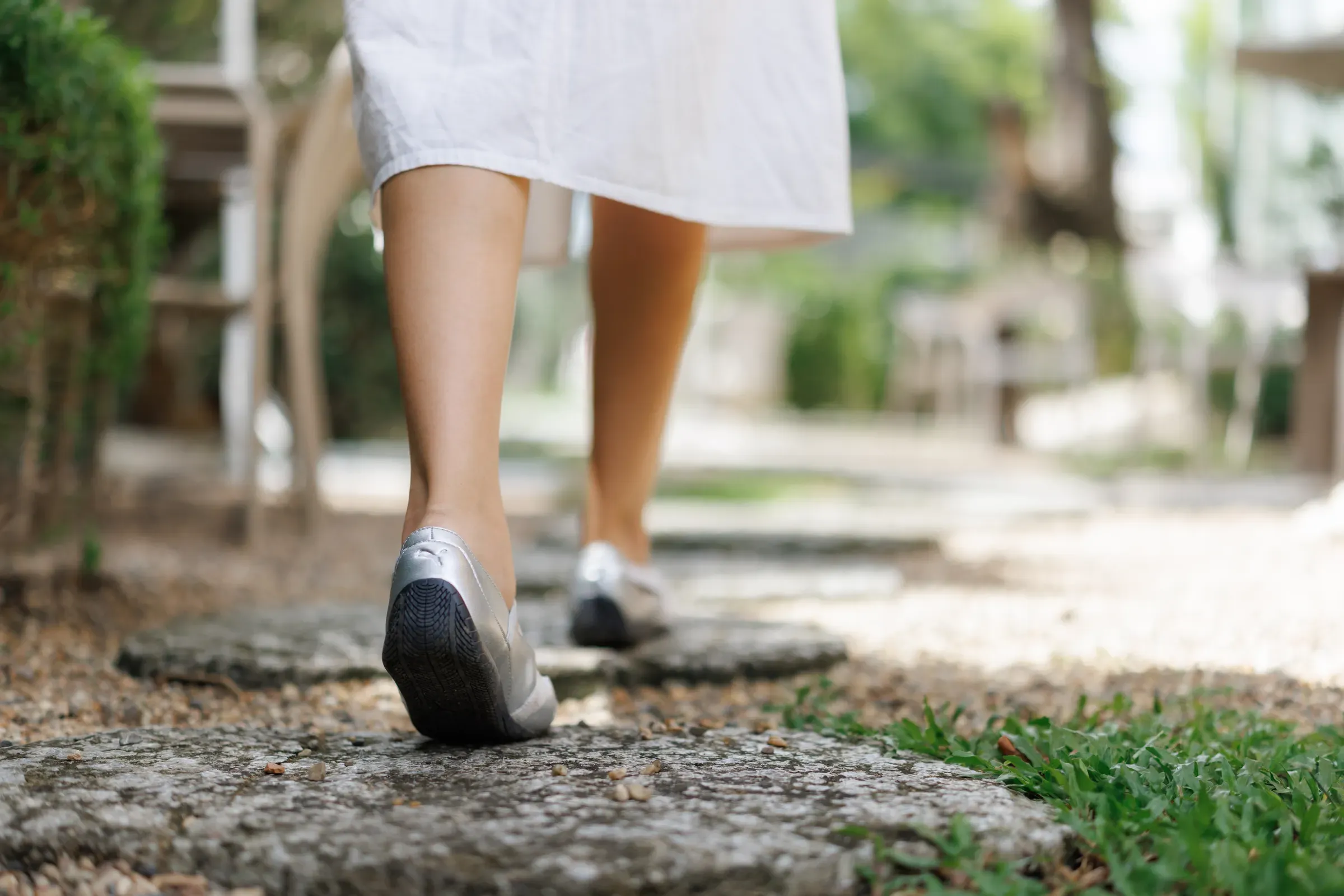 Woman walking on stone path in garden wearing silver shoes, orthopedic & comfort footwear ecommerce