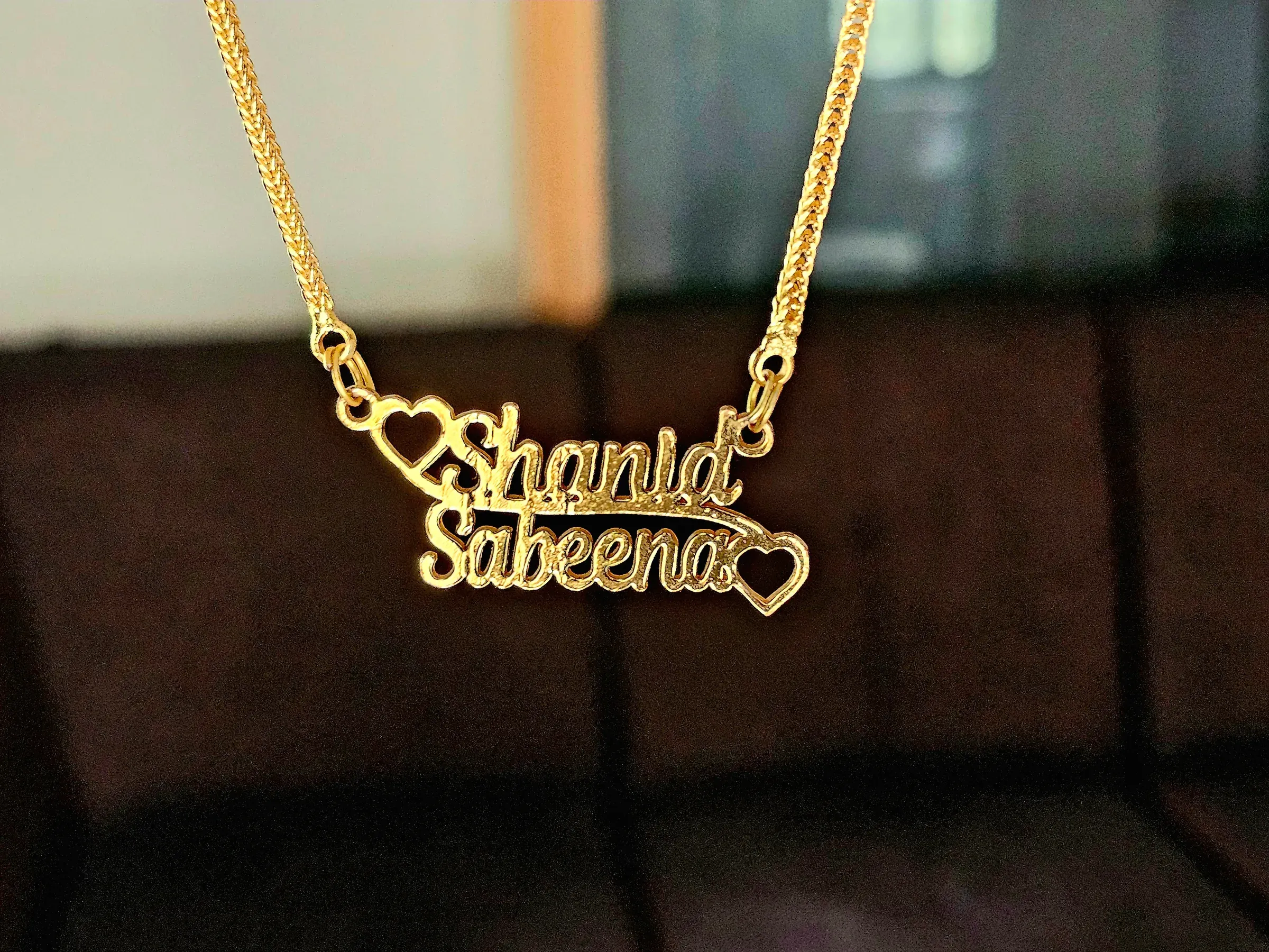 Gold necklace featuring a custom two-name pendant reading "Shanid" and "Sabeena" with heart accents, personalized jewelry ecommerce
