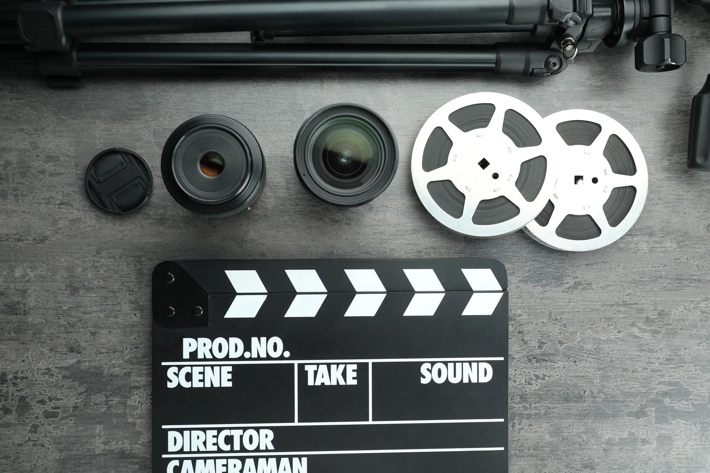 Flat lay composition with movie clapper, film reels and camera lens on grey textured table, photography accessories ecommerce