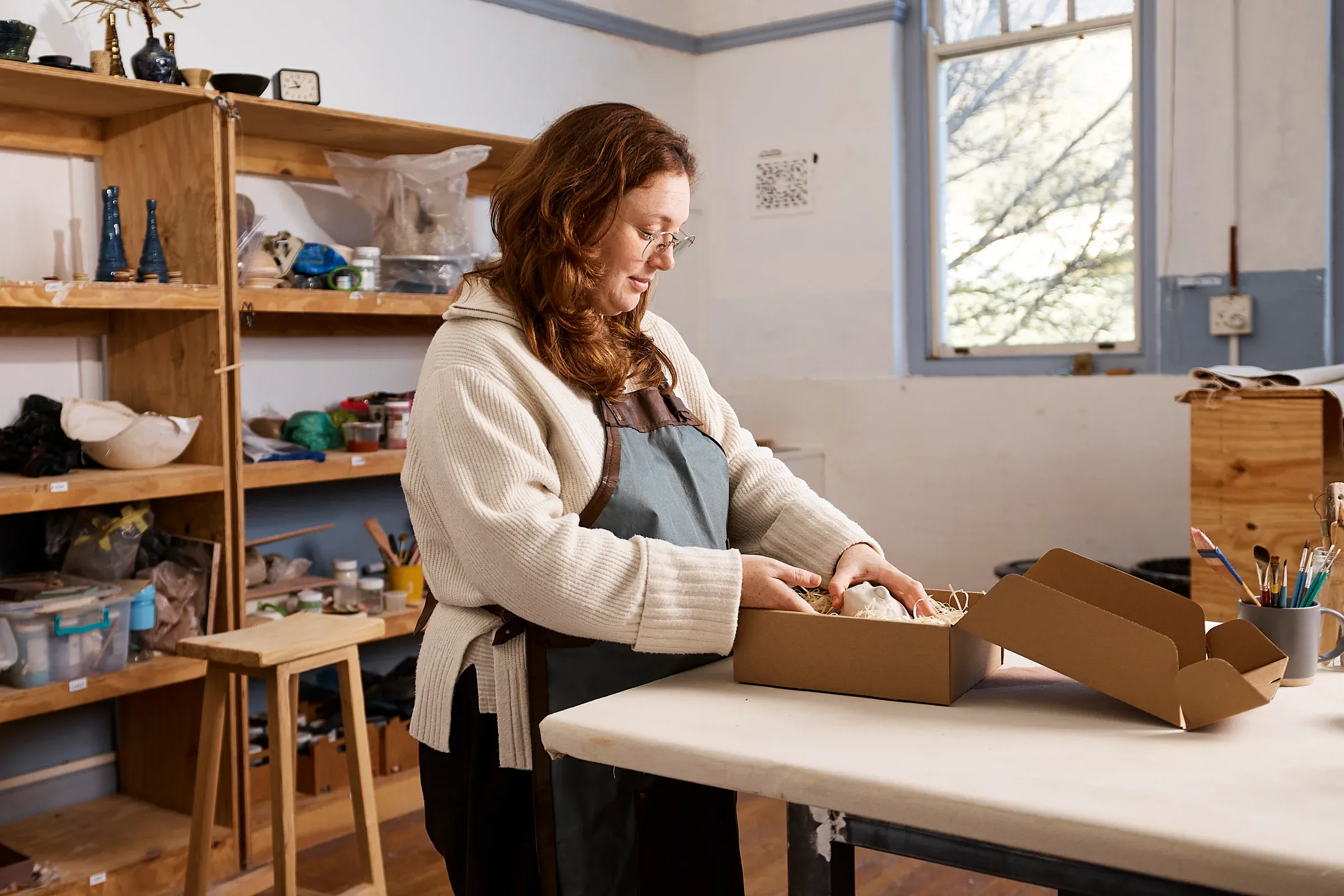 A potter wrapping handmade ceramics into a shipping box in her studio