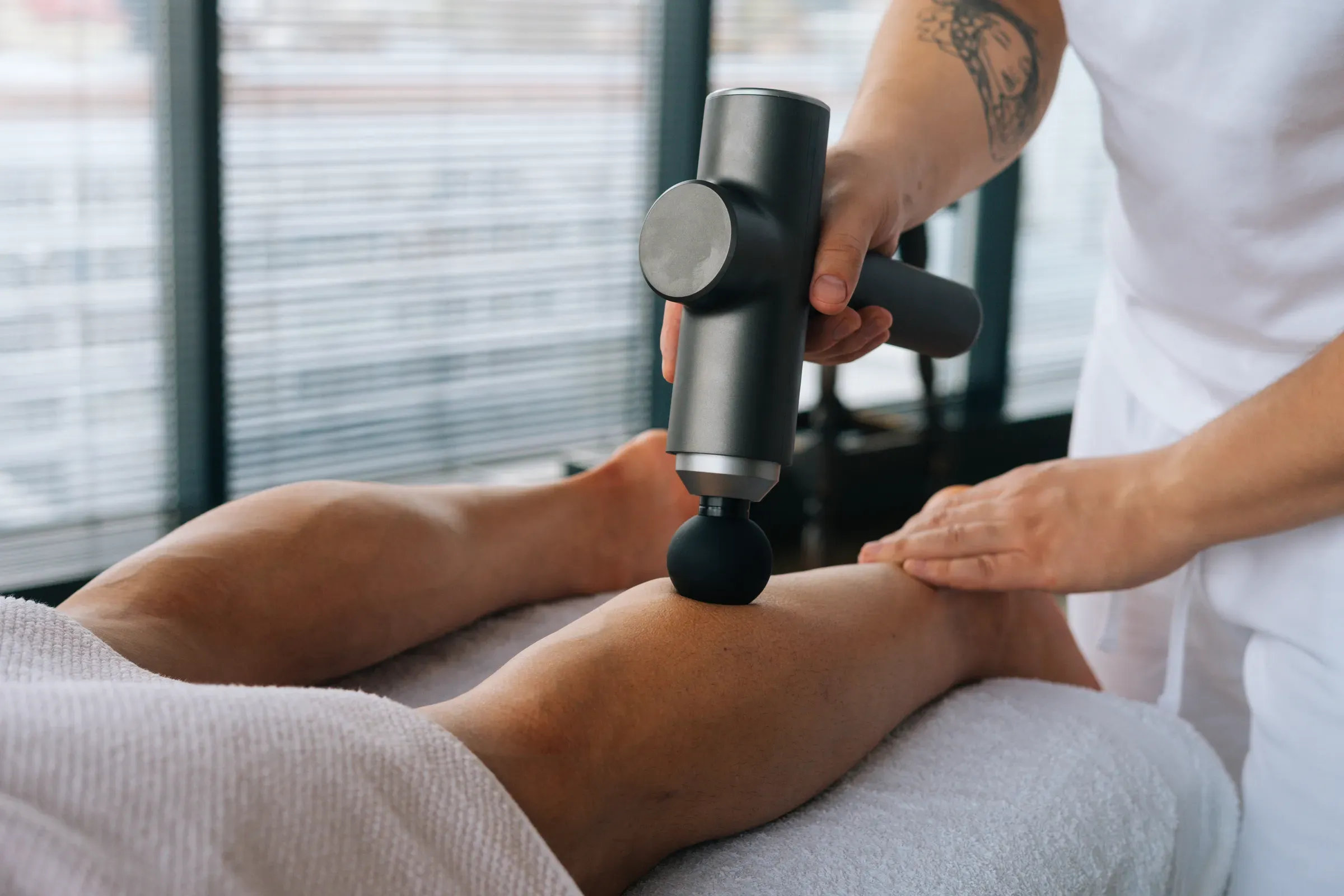 Close-up of unrecognizable professional male masseur massaging leg calf muscles using massage gun percussion, recovery & mobility devices ecommerce