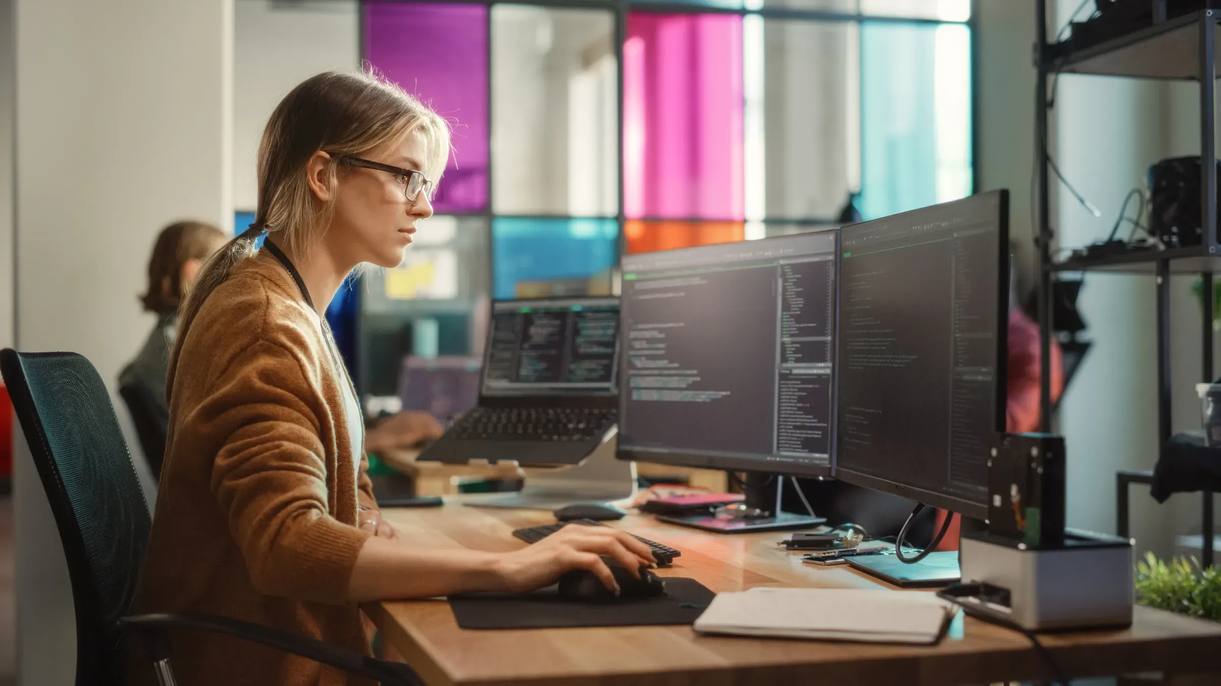 Caucasian Woman Coding on Desktop PC and Laptop Setup With Multiple Displays in Spacious Office. Female, stores replatforming ecommerce