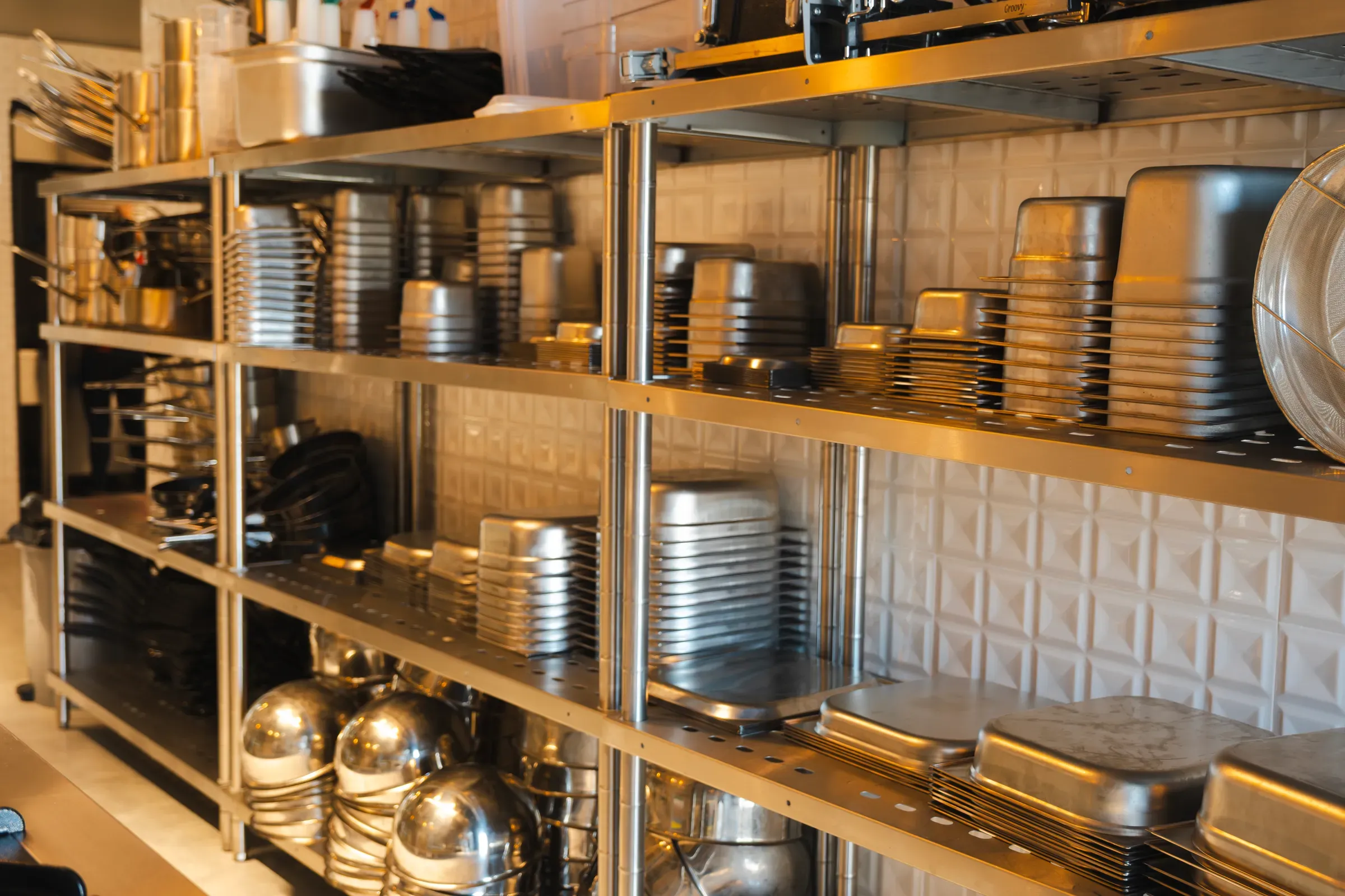 Stainless steel shelves displaying precisely stacked bakeware, pans, and other kitchen equipment, creating an, restaurant & foodservice supply ecommerce