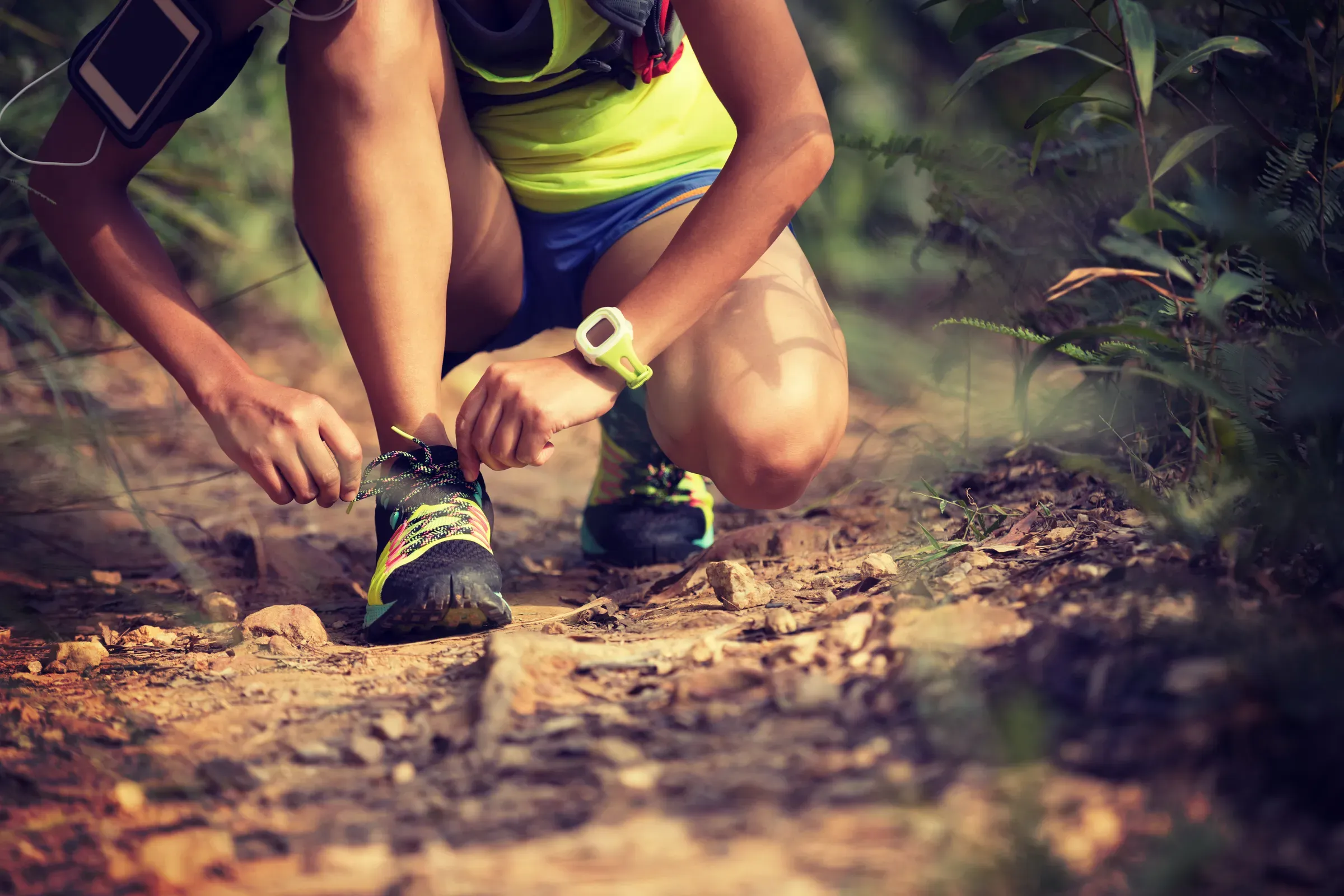 Young woman ultra marathon runner tying shoelace on forest trail, running & triathlon gear ecommerce