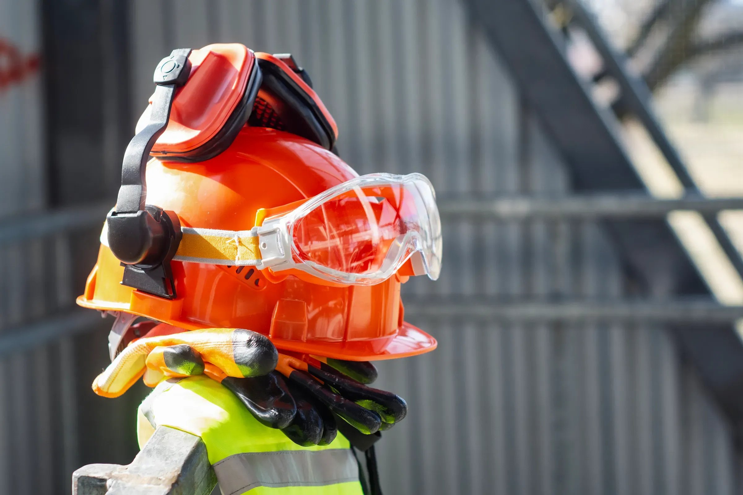 Construction safety helmet with protective goggles, ear protection and work gloves at building site. Personal, safety & ppe ecommerce