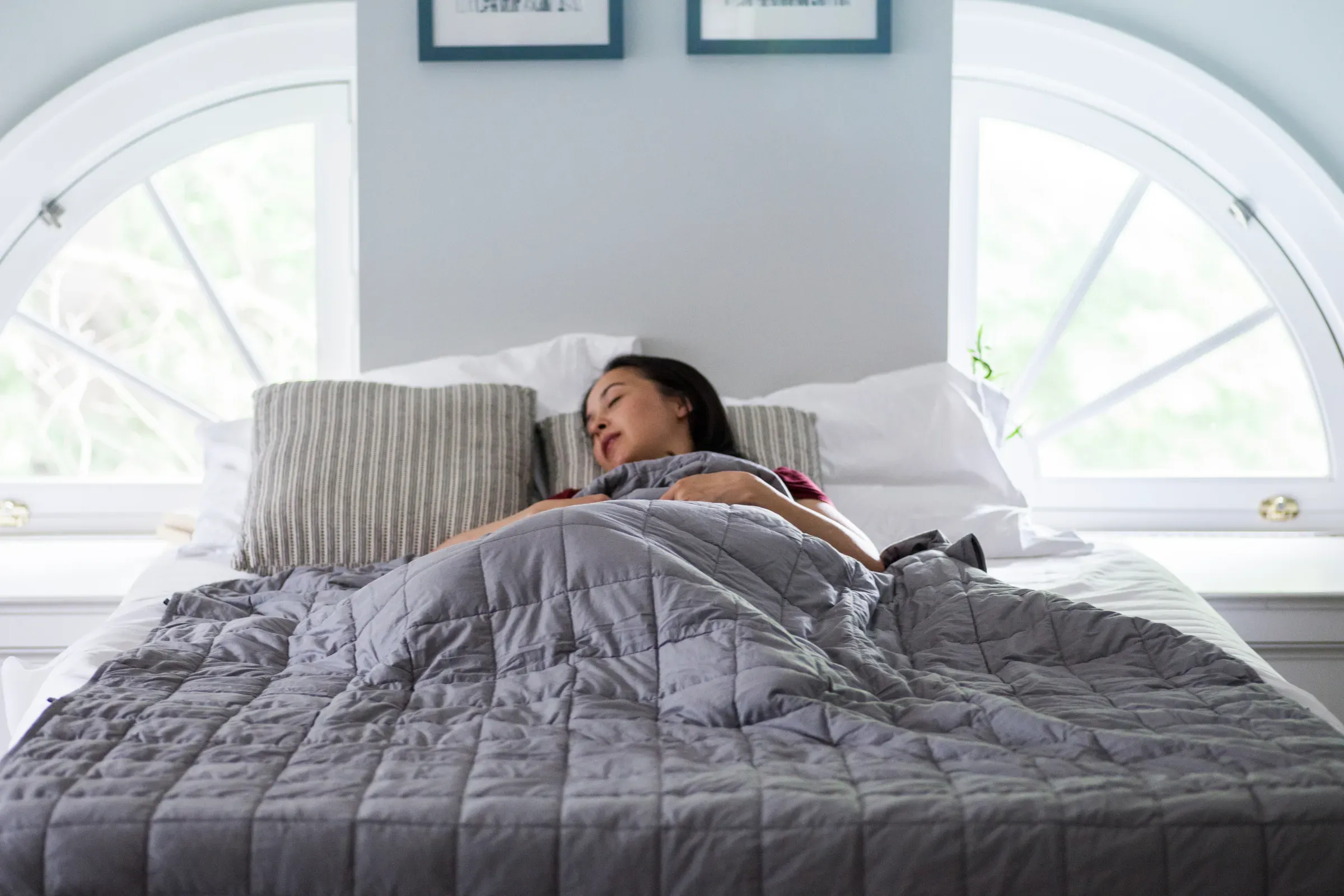 Woman sleeps under weighted blanket in bright bedroom, sleep products ecommerce