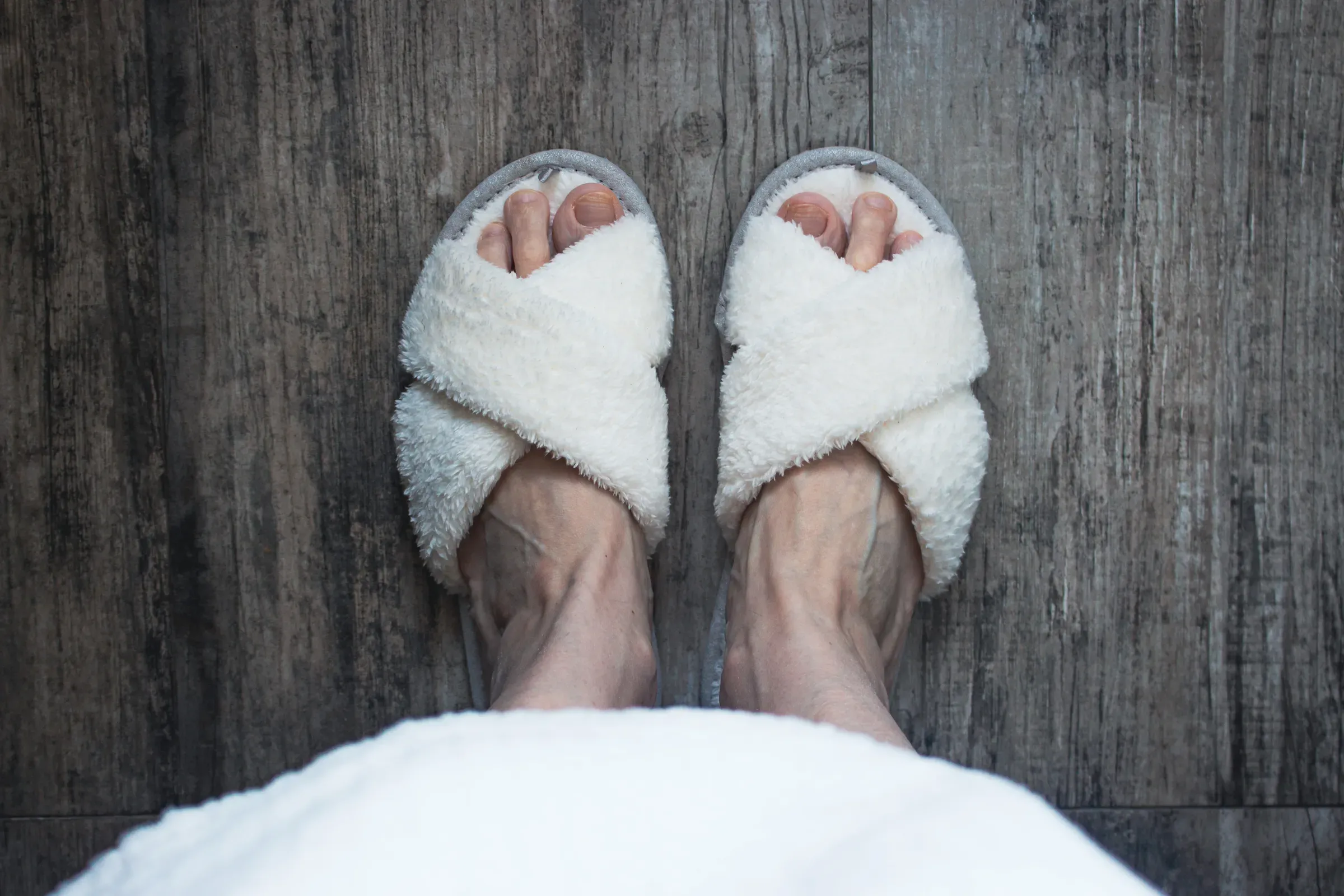 White soft slippers on women feet, top view. Homey clothing. Cozy fluffy slippers on legs, view from above., slippers ecommerce