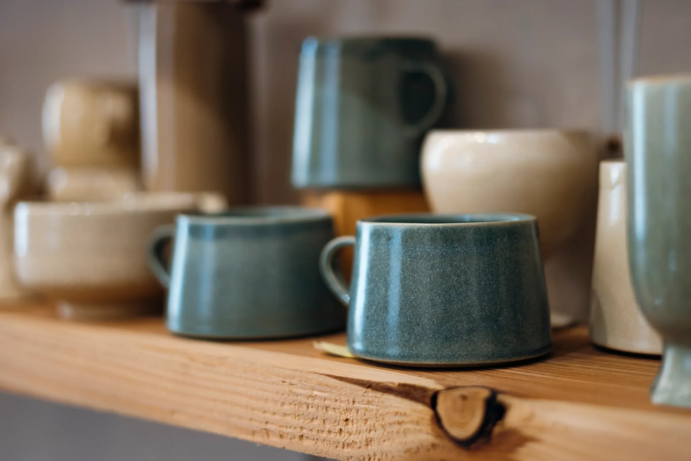 Handmade stoneware mugs lined up on a wooden shelf in a pottery shop