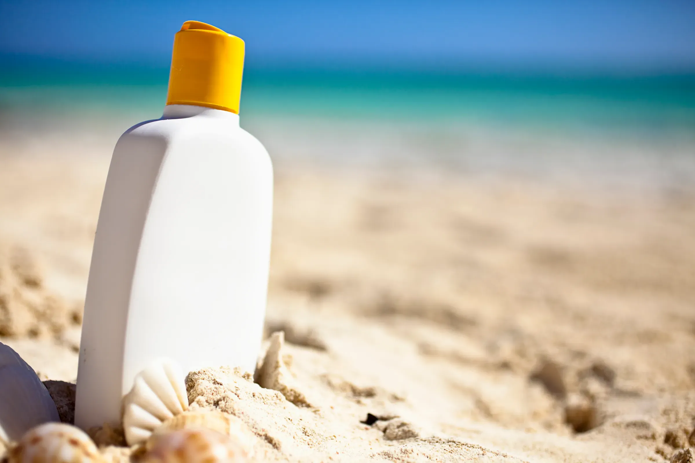 White bottle of sunscreen resting in the sand at the beach, sunscreen & spf ecommerce