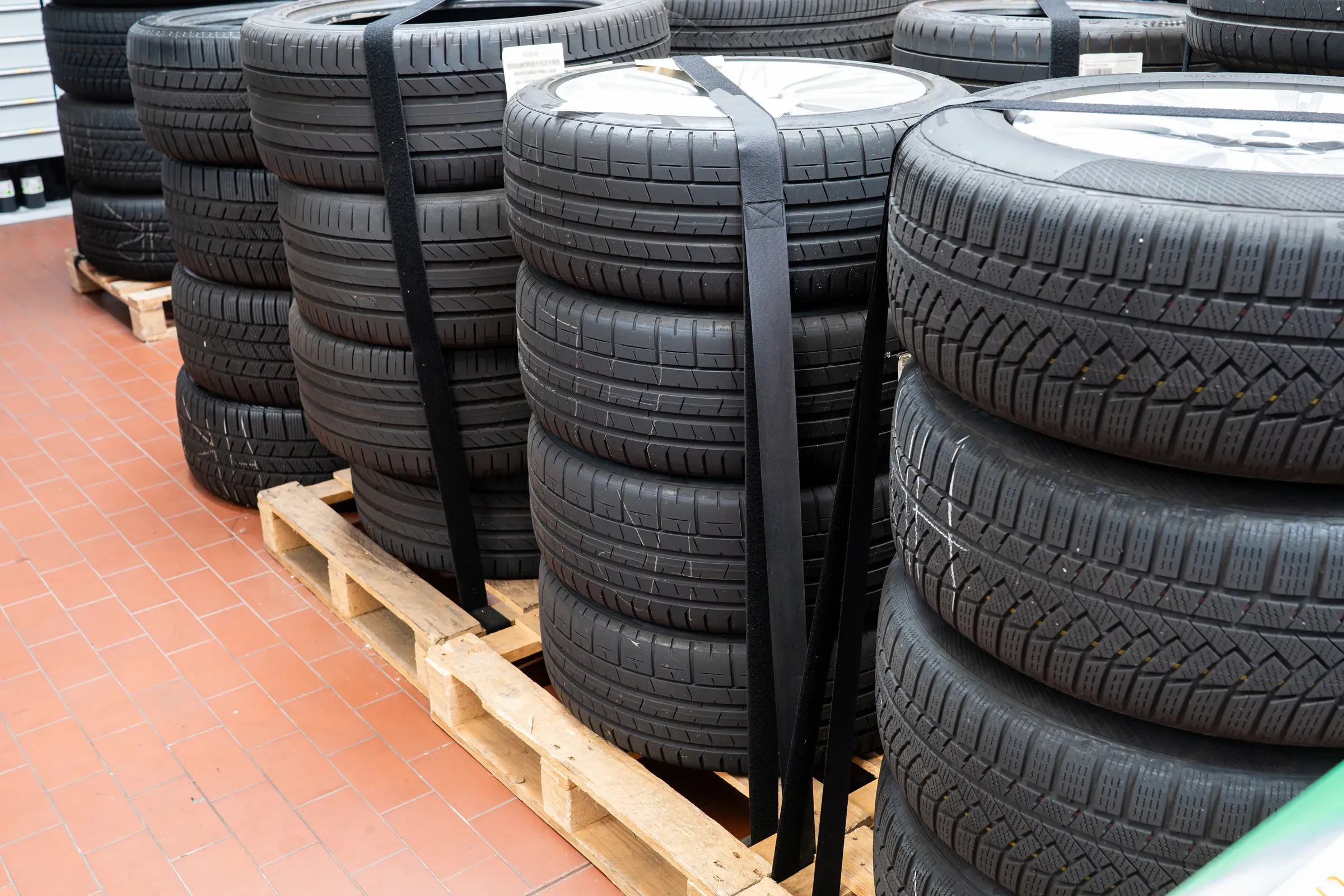 New car tires mounted on alloy wheels stacked inside a car repair shop. Close up, wide angle view, no people, tires & wheels ecommerce