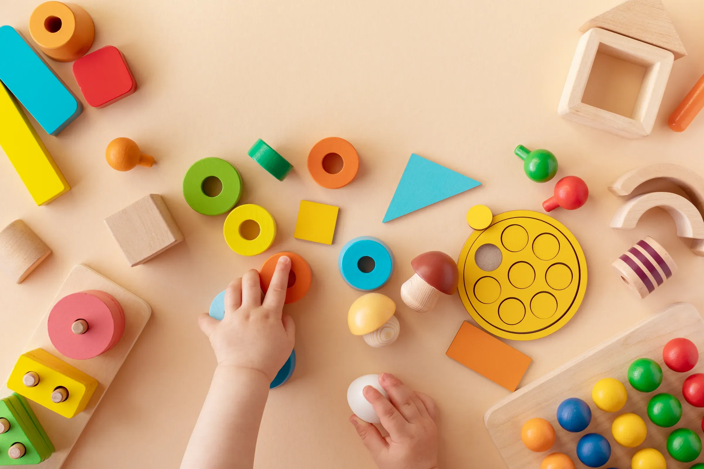 Toddler activity for motor and sensory development. Baby hands with colorful wooden toys on table from above, toys ecommerce