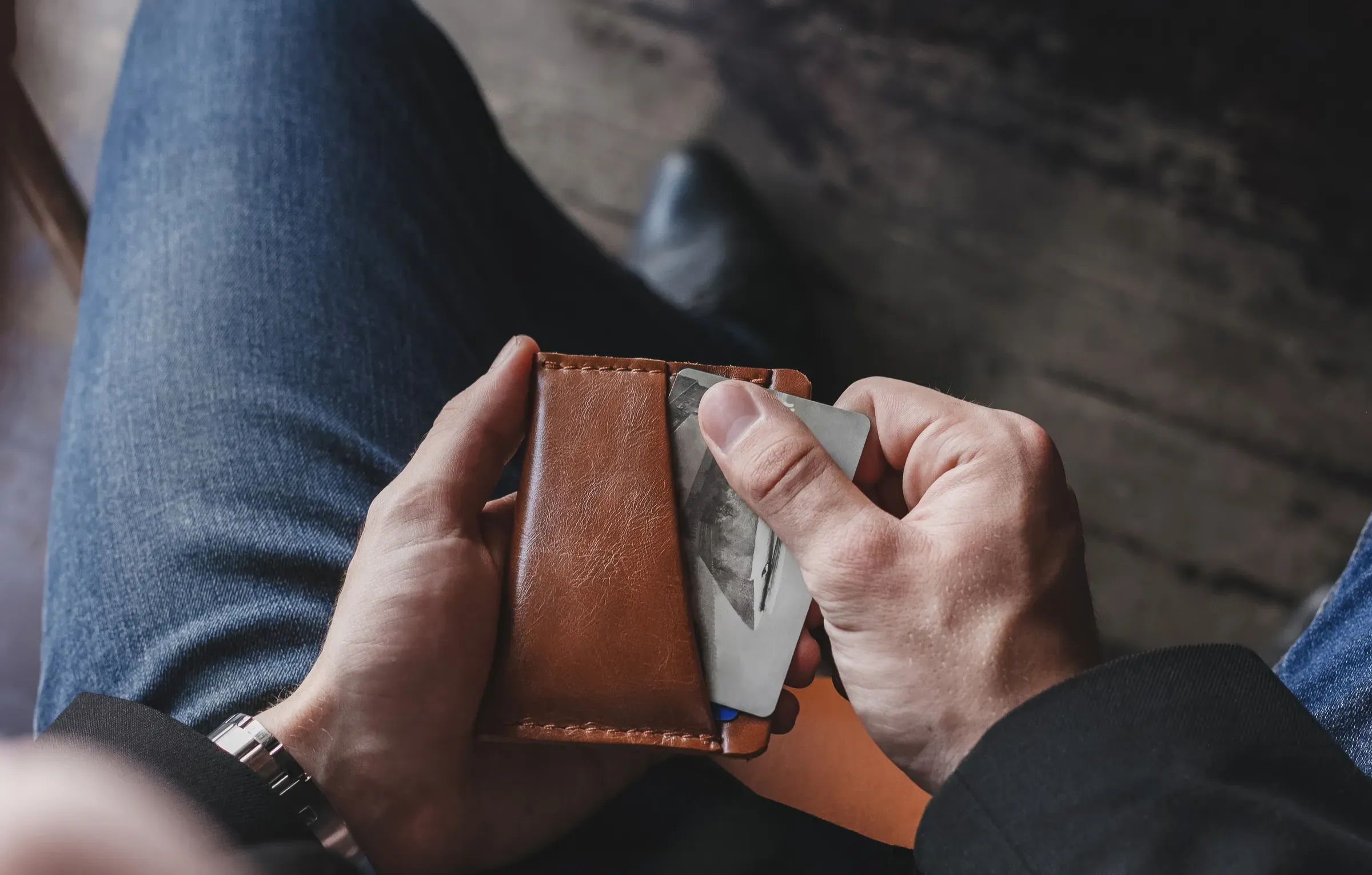 A man takes out credit cards from a brown leather wallet on a dark background, wallets & cardholders ecommerce