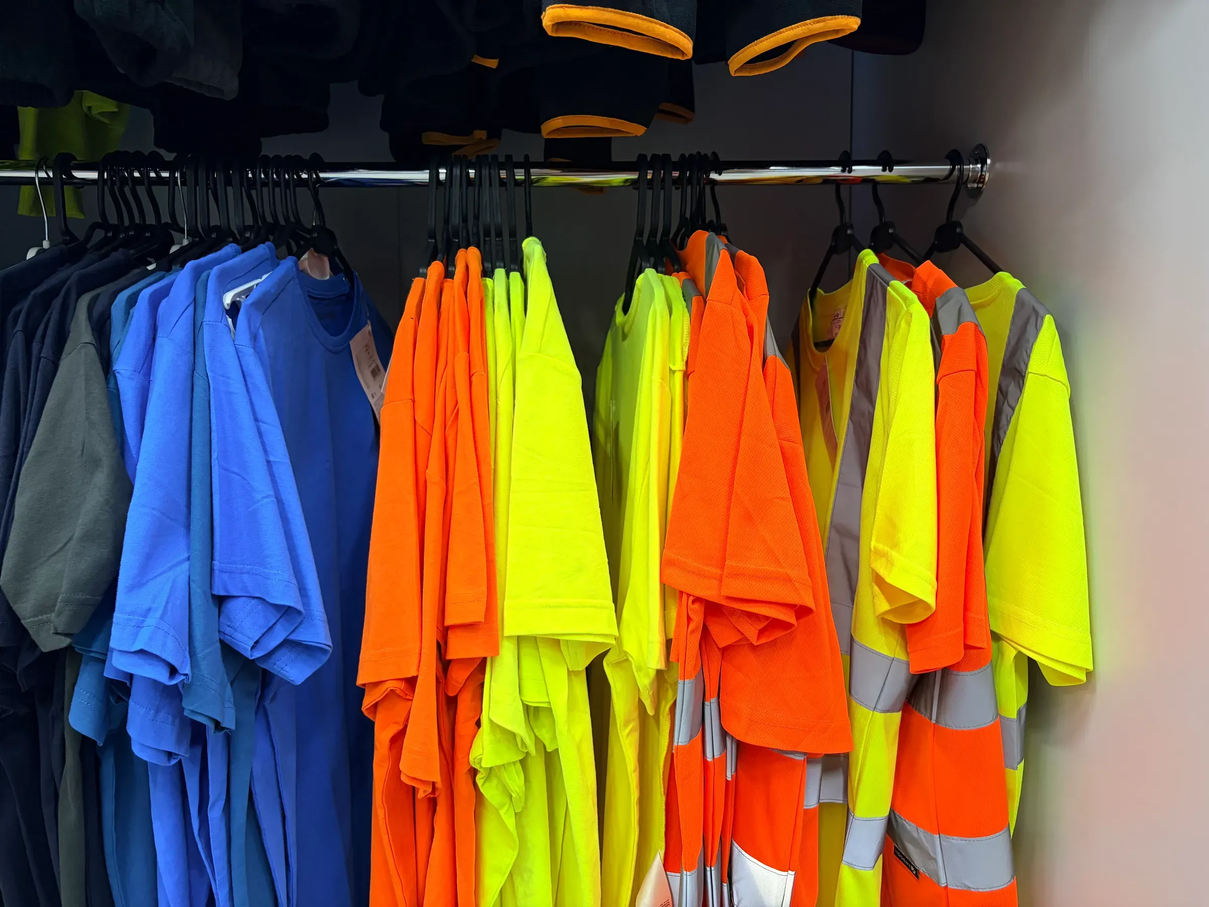Rack of colorful workwear including high-visibility safety vests and t-shirts in a closet, workwear & uniforms ecommerce